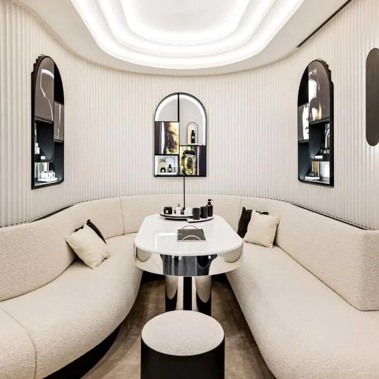 Consultation room at Maison de Beauté Carita, with curved cream seating, a central table and arched product displays.