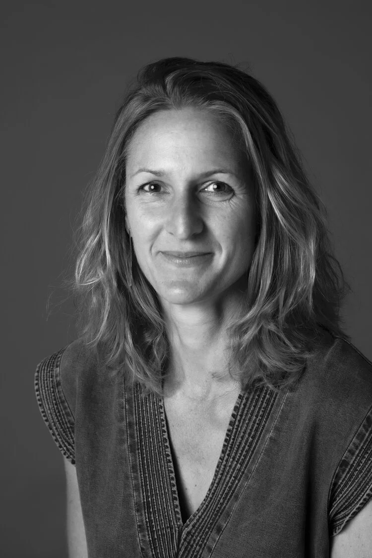 Black and white portrait of a smiling woman with wavy hair, wearing earrings and a necklace with a butterfly pendant, against a plain background.