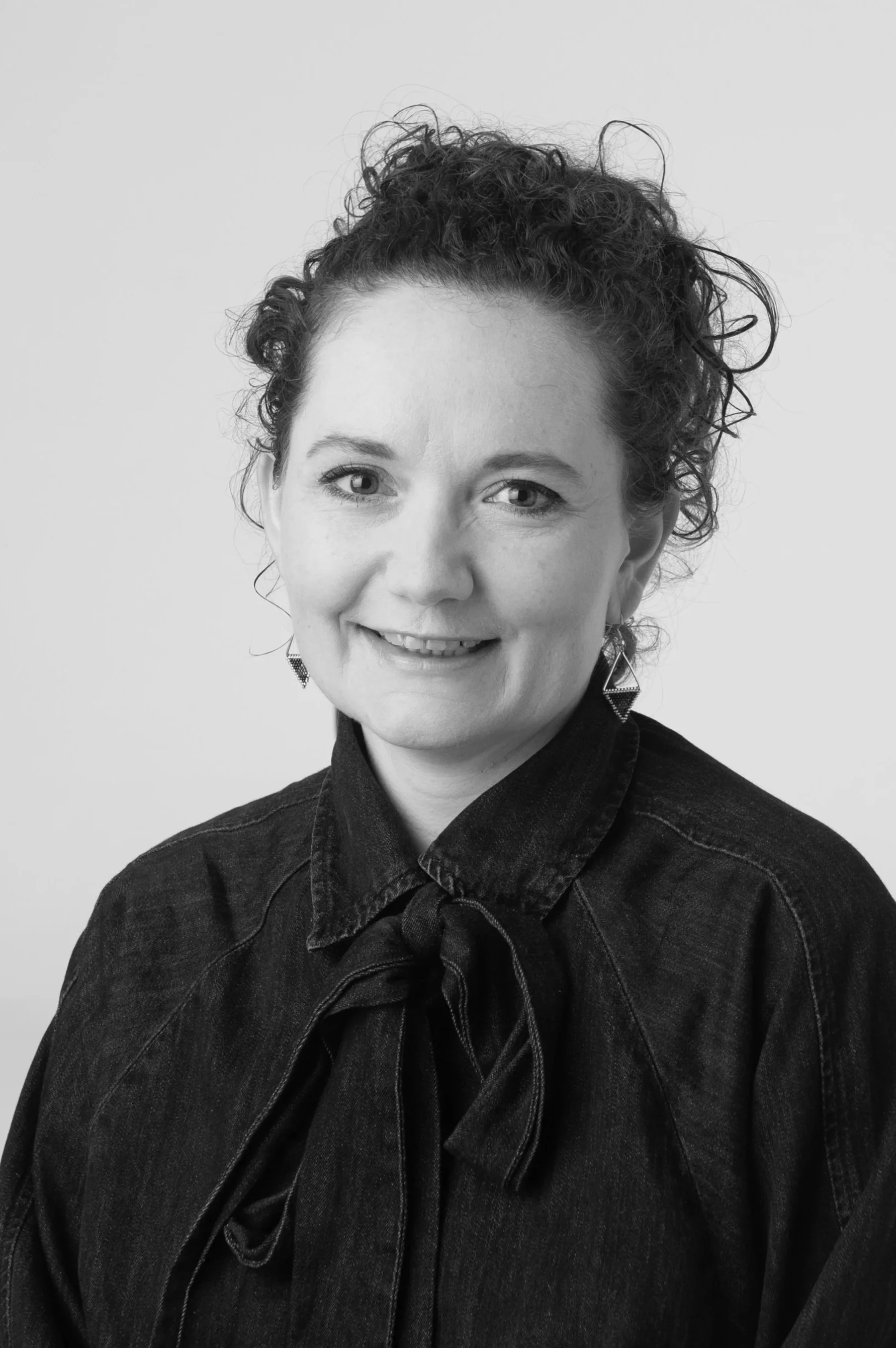 Black and white portrait of a woman with curly hair wearing a sleeveless polka dot top, looking directly at the camera.