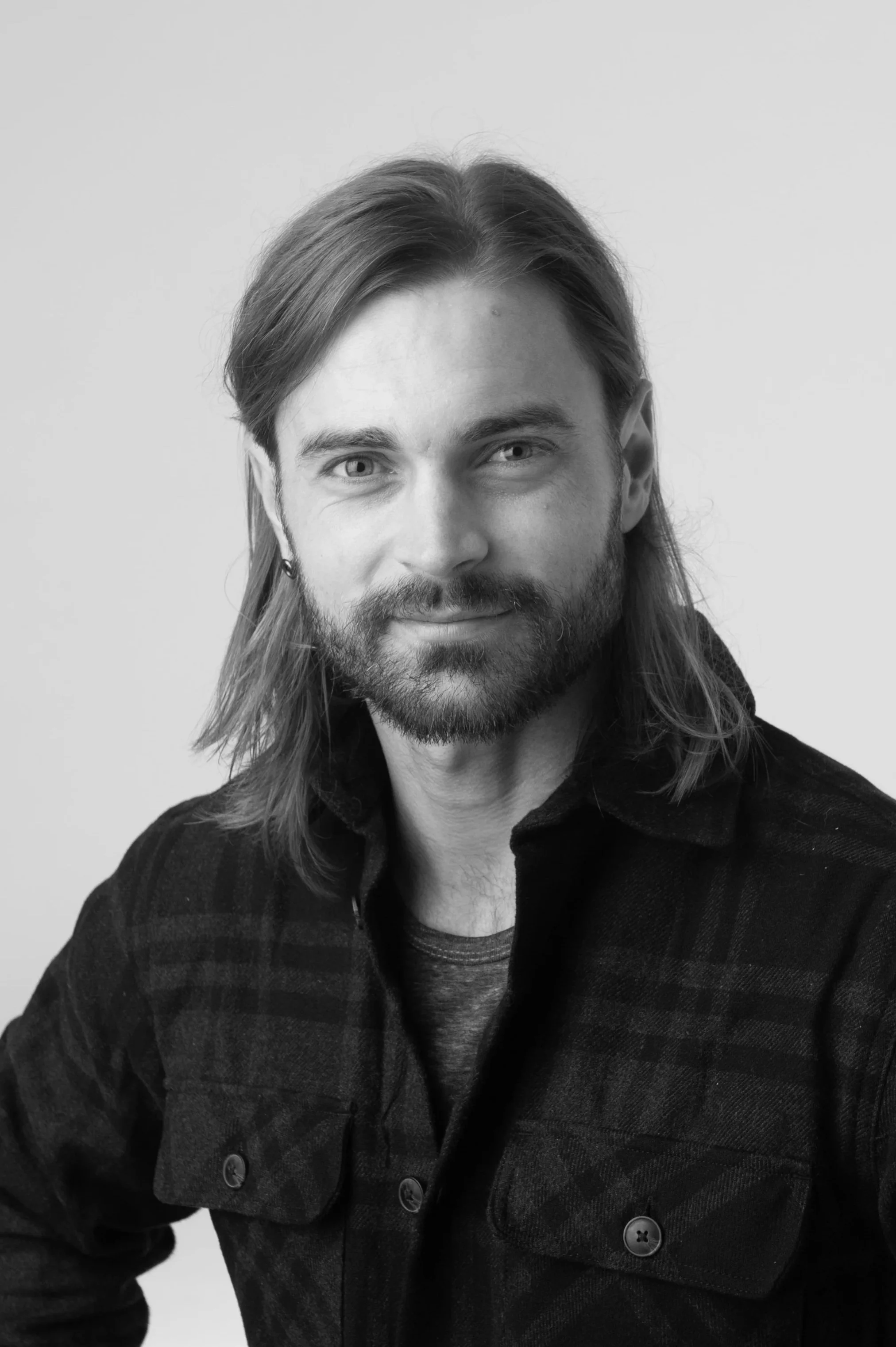 Black and white portrait of a man with glasses, a beard, and a mustache wearing a dark plaid shirt, looking directly at the camera.