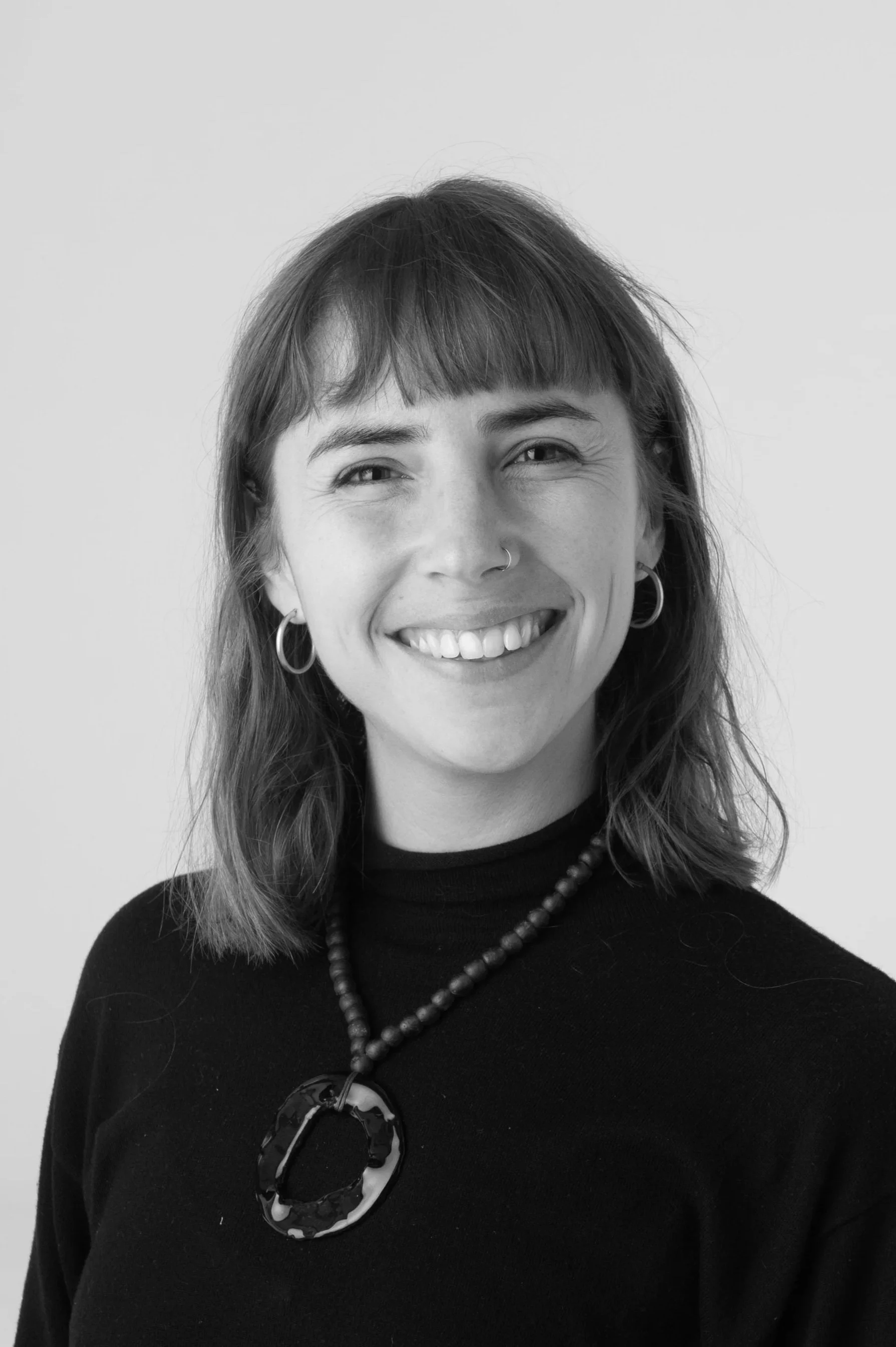 Black and white portrait of a woman smiling, wearing earrings, a nose ring, and a blouse with a black ribbon tie.