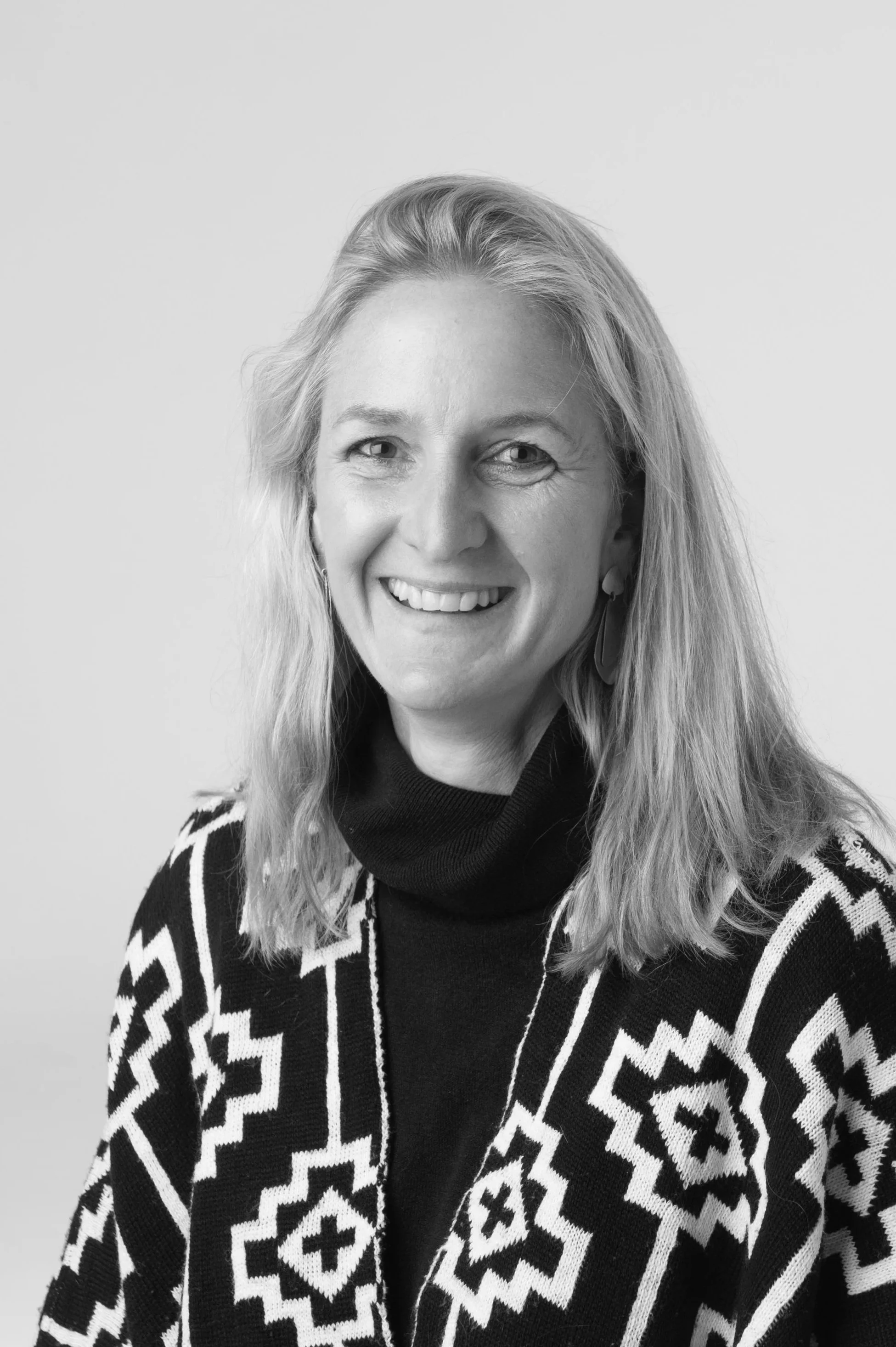 Black and white portrait of a smiling woman with wavy hair, wearing earrings and a necklace with a butterfly pendant, against a plain background.