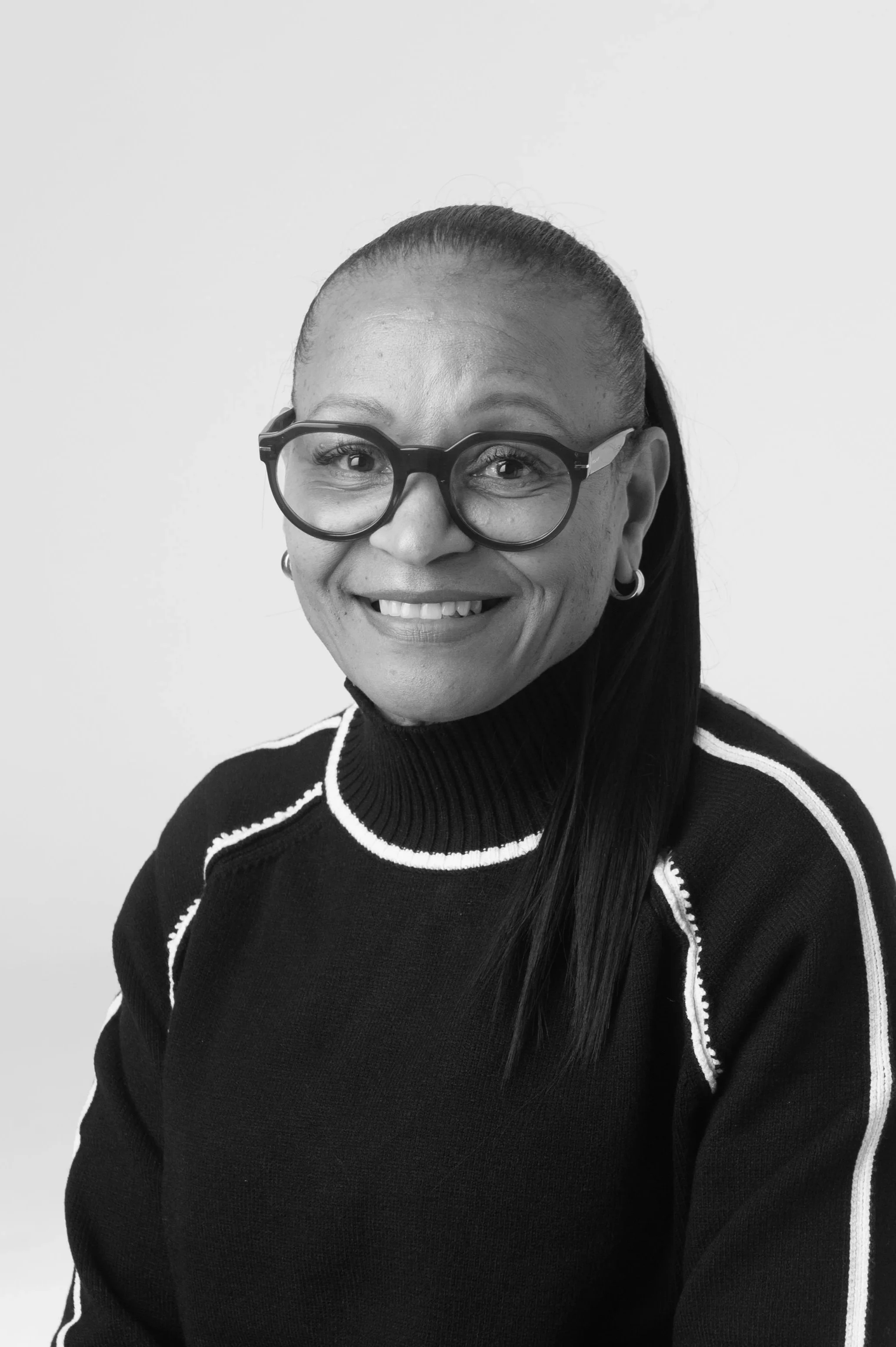 Black and white portrait of a smiling woman wearing glasses and a sleeveless top with a horizontal white stripe.