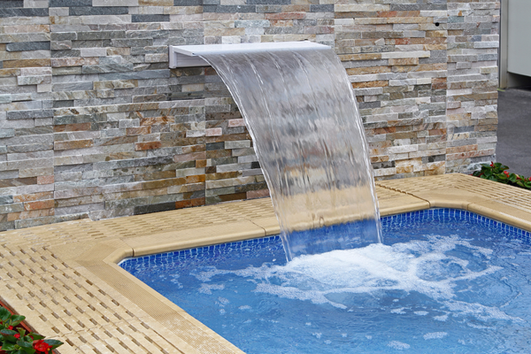 A beautiful backyard spa with a brick accent wall and fountain.