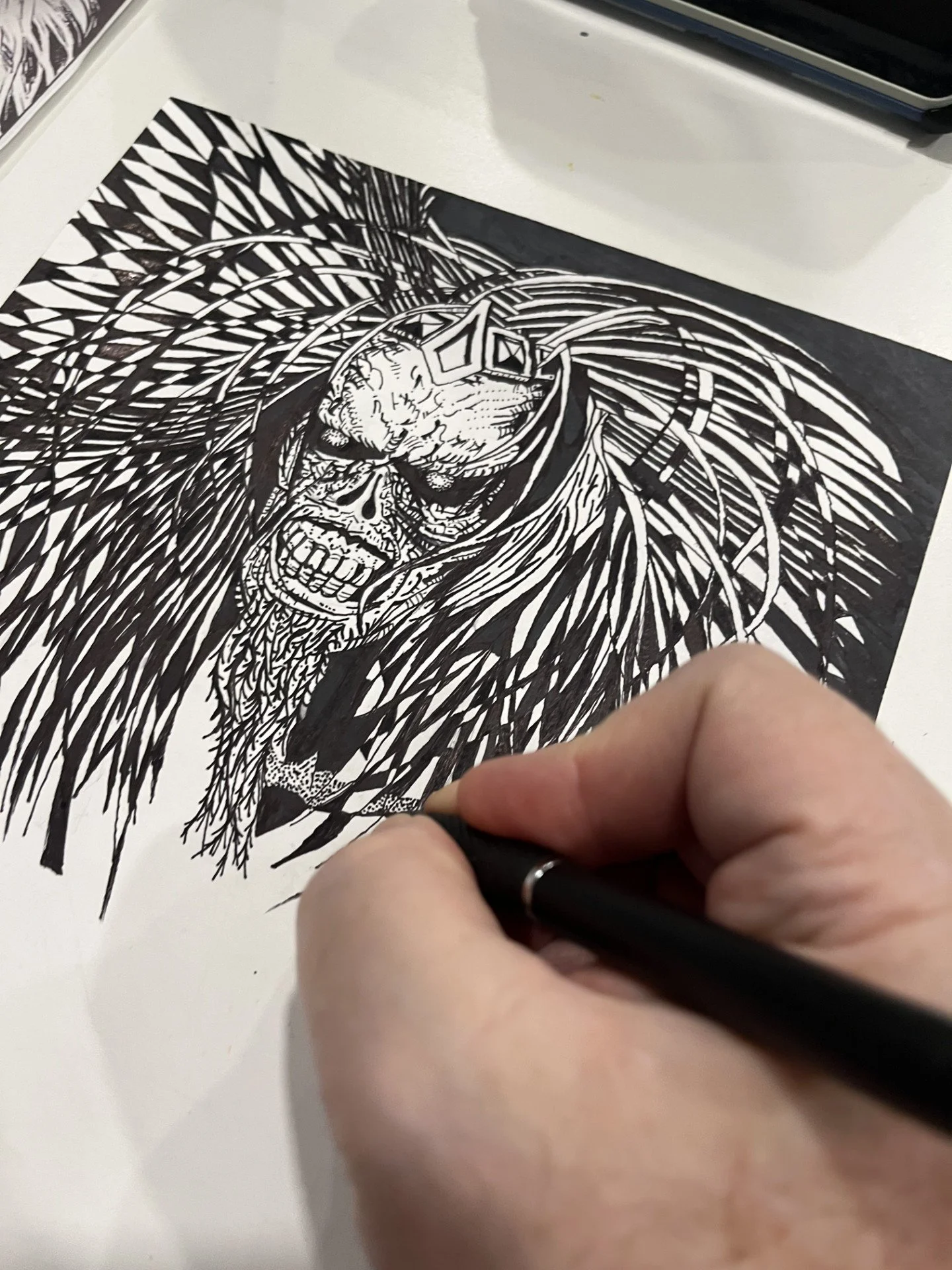 A person creating a detailed black and white ink drawing of a skull with intricate patterns and abstract lines.