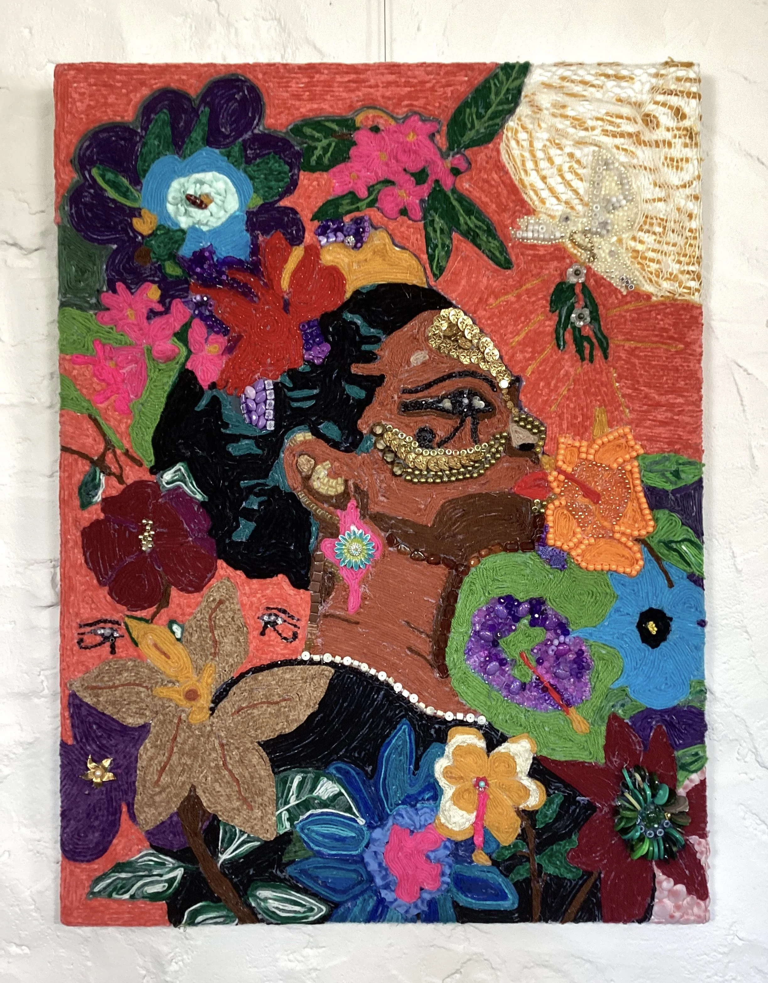 A colorful mosaic of various buttons, beads, and embellishments arranged to form a portrait of a woman with black hair, blue eyes, and a warm complexion.