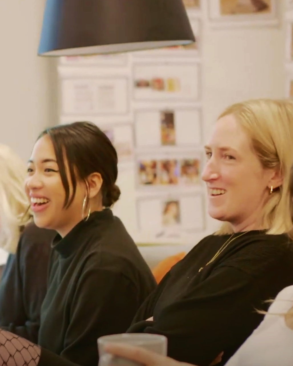 Two women sitting and smiling at a social gathering in a cozy indoor space.