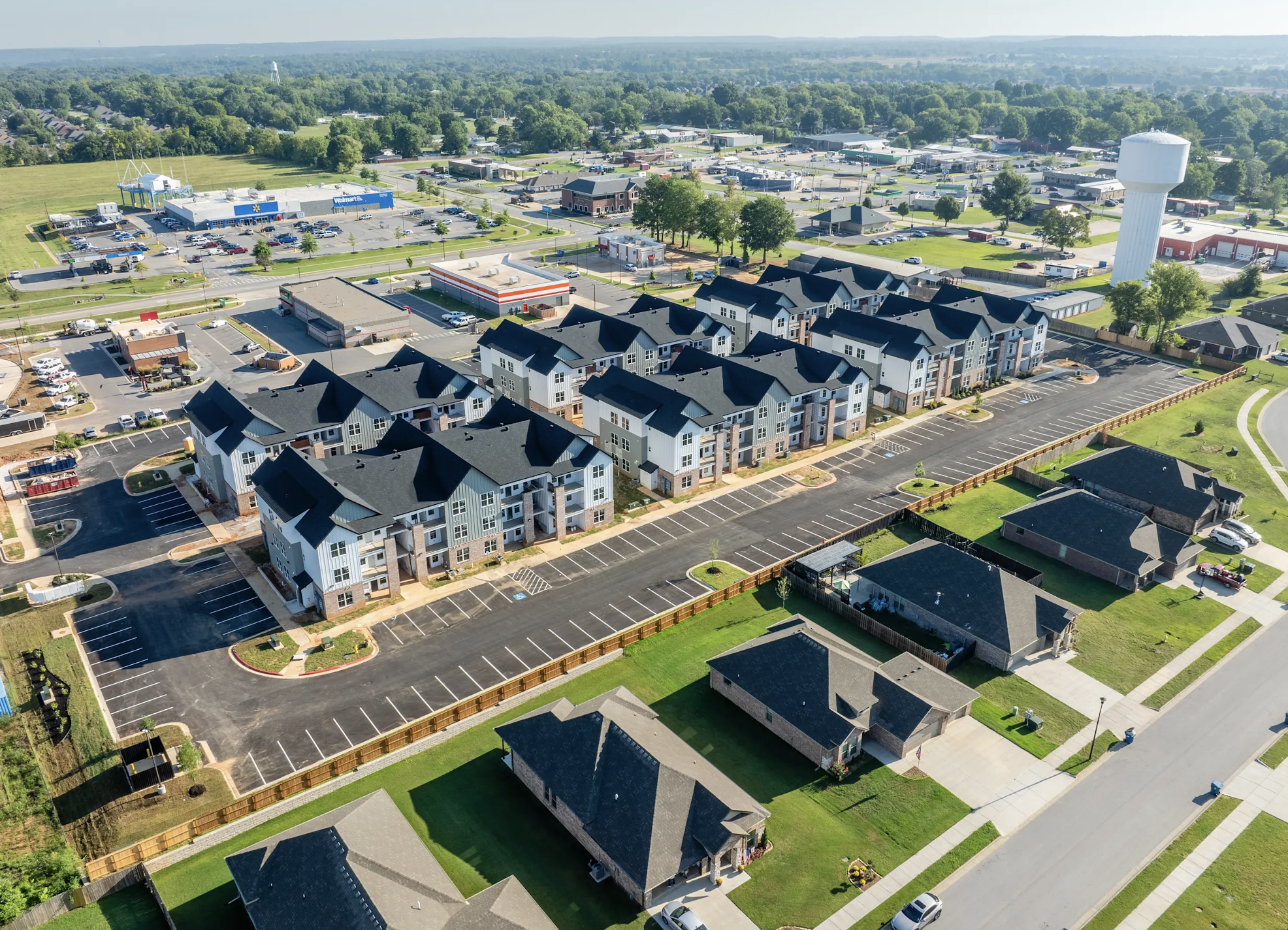 Aerial view of a neighborhood with apartment buildings, parking lots, and surrounding houses in a suburban area.