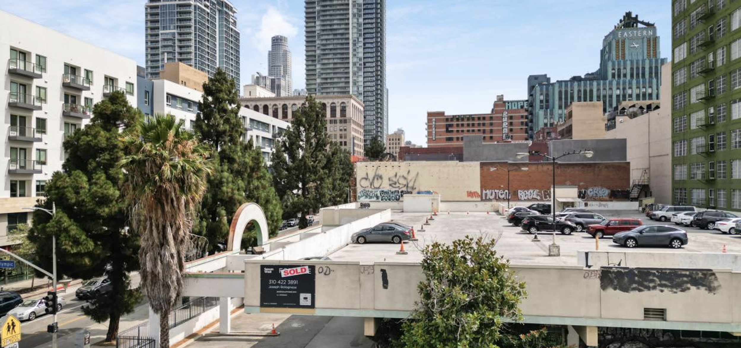 Downtown Los Angeles parking lot with cars, palm trees, and tall buildings in the background.