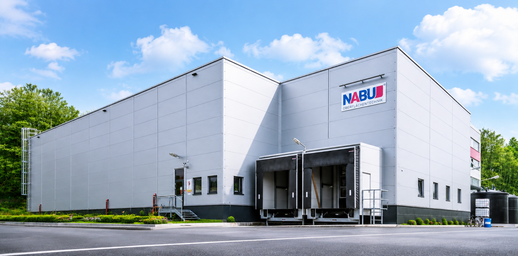 xterior view of the modern grey NABU Oberflächentechnik facility featuring company branding, loading bays, and surrounding greenery