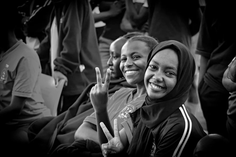 People seated together, with two smiling and making peace signs.