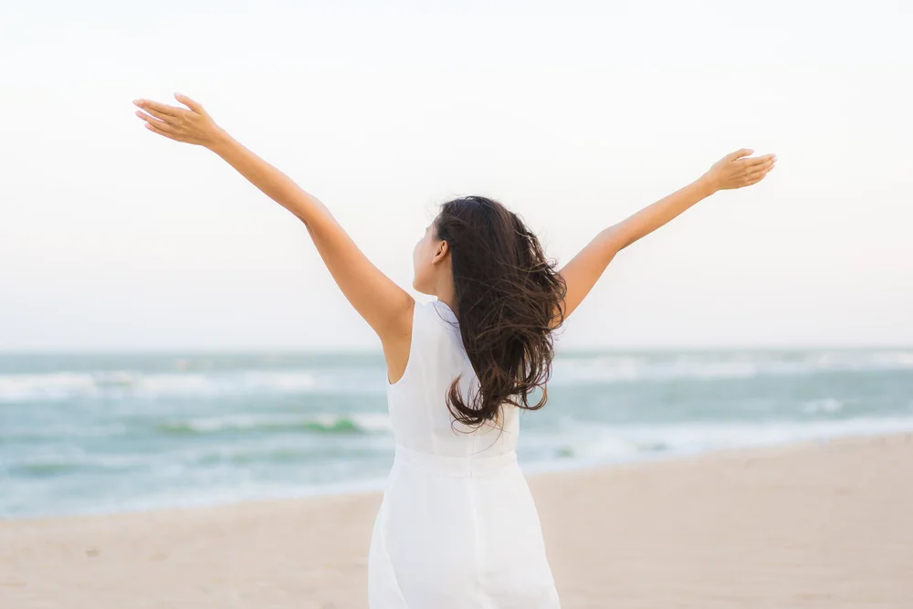 A person facing the ocean with their arms outstretched.