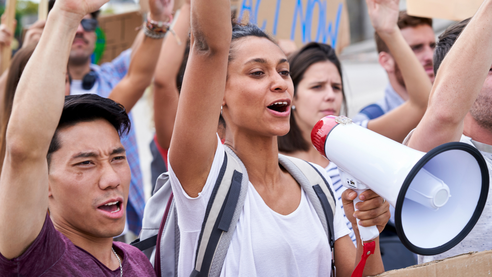 A person holding a megaphone among a crowd with raised arms.