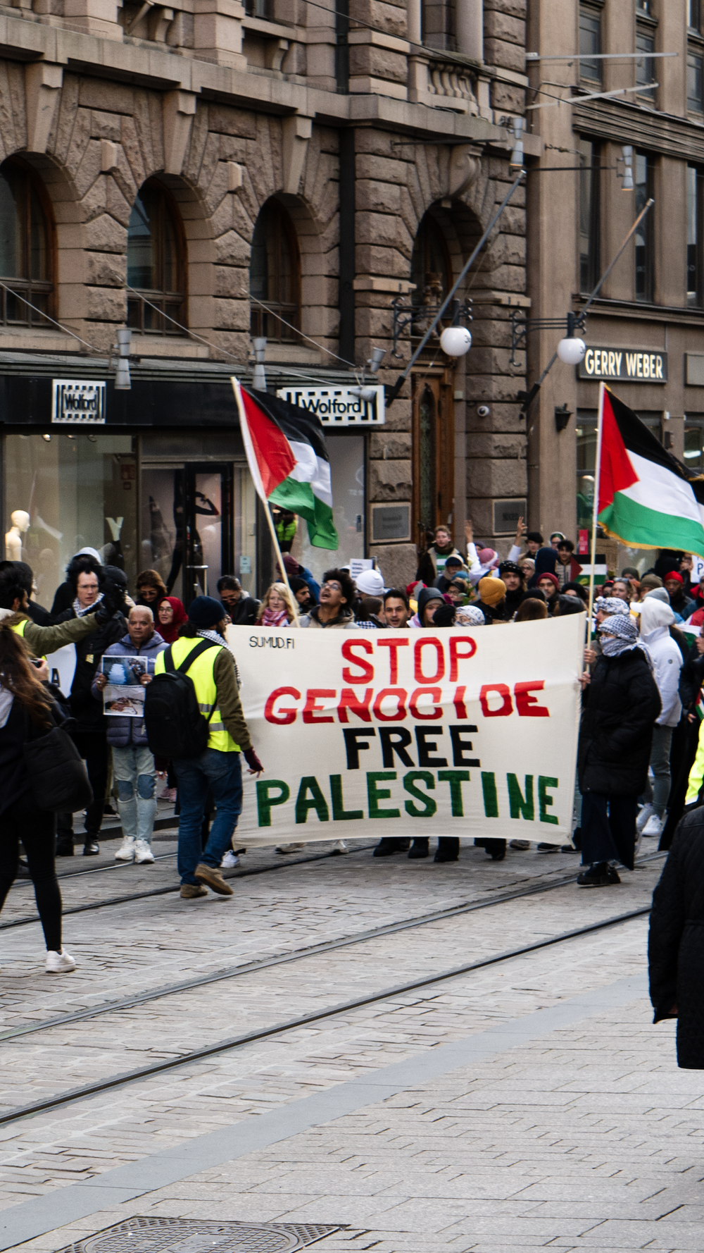 Marchers carrying Palestinian flags and a banner reading 'Stop Genocide, Free Palestine'.