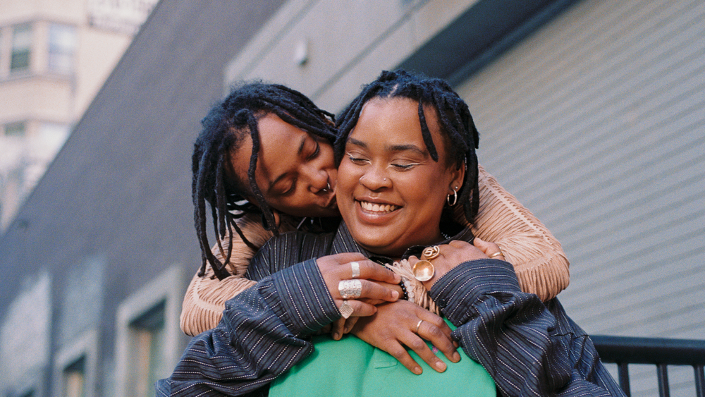 Two people embracing outdoors, one kissing the other's cheek.
