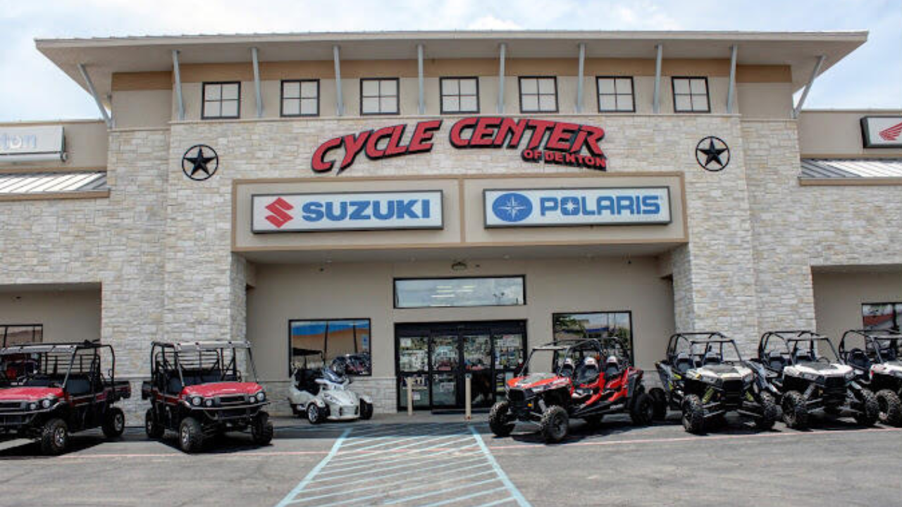 Exterior view of a vehicle dealership with signages for Cycle Center of DeKalb, Suzuki, and Polaris, displaying several off-road vehicles and golf carts parked in front.