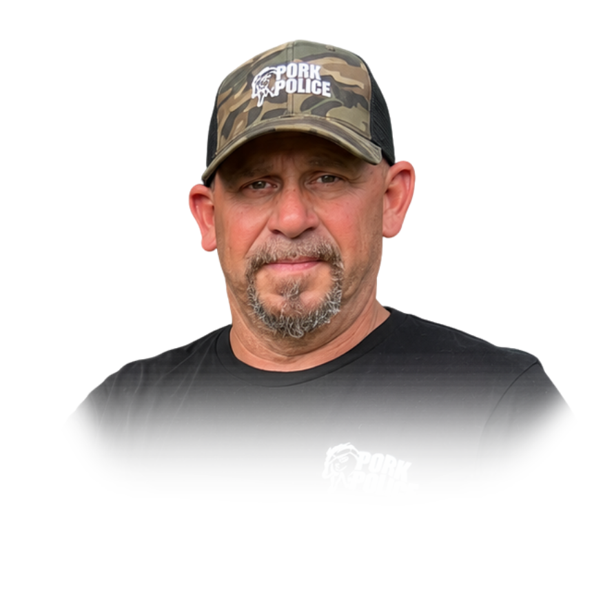 A man wearing a camouflage cap with 'Pork Police' logo and a black T-shirt with the same logo, posing outdoors.
