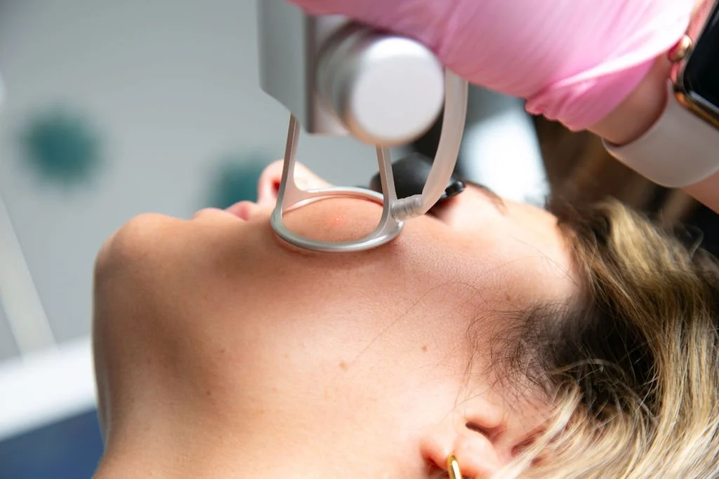 A woman undergoes a skincare treatment using a specialized device on her face in a medical or aesthetic clinic.