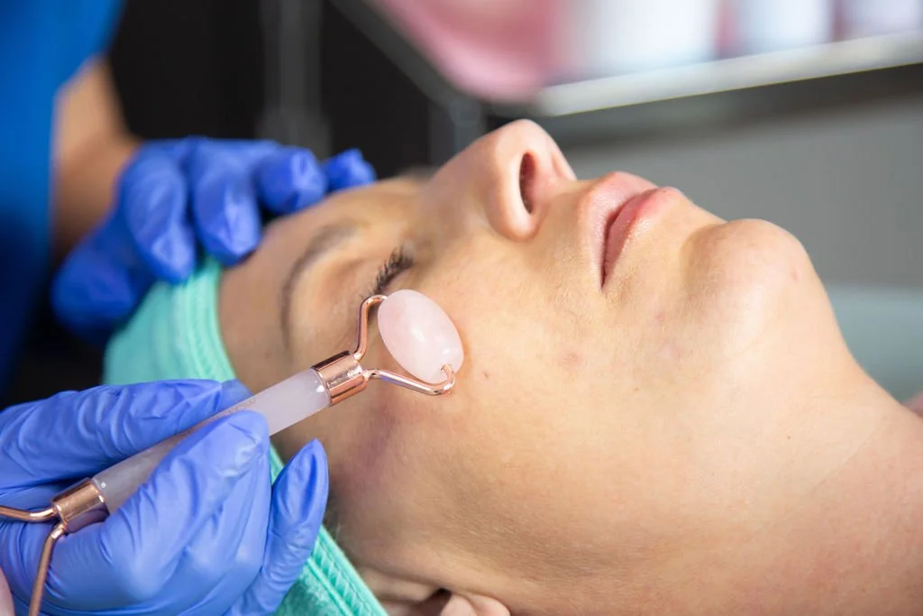 A woman receiving a facial treatment with a jade roller at a spa or clinic.