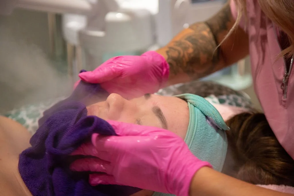 A healthcare professional wearing pink gloves tending to a patient lying on a hospital bed, with the patient's face covered by a mask.