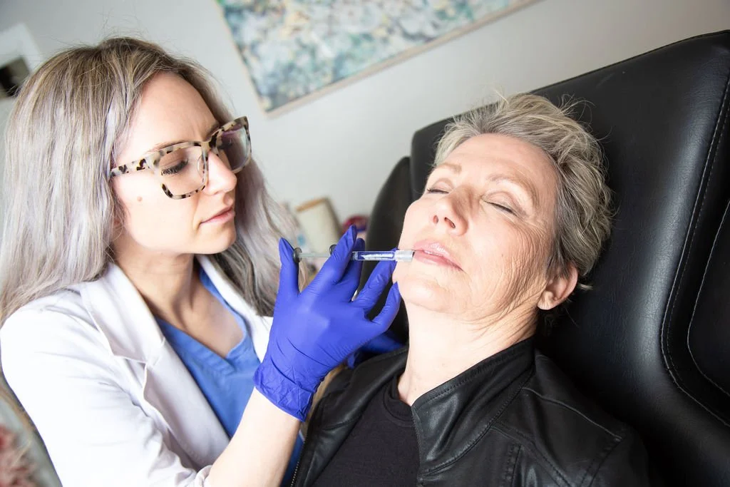 A healthcare professional administering a cosmetic injection to an older woman's lips.