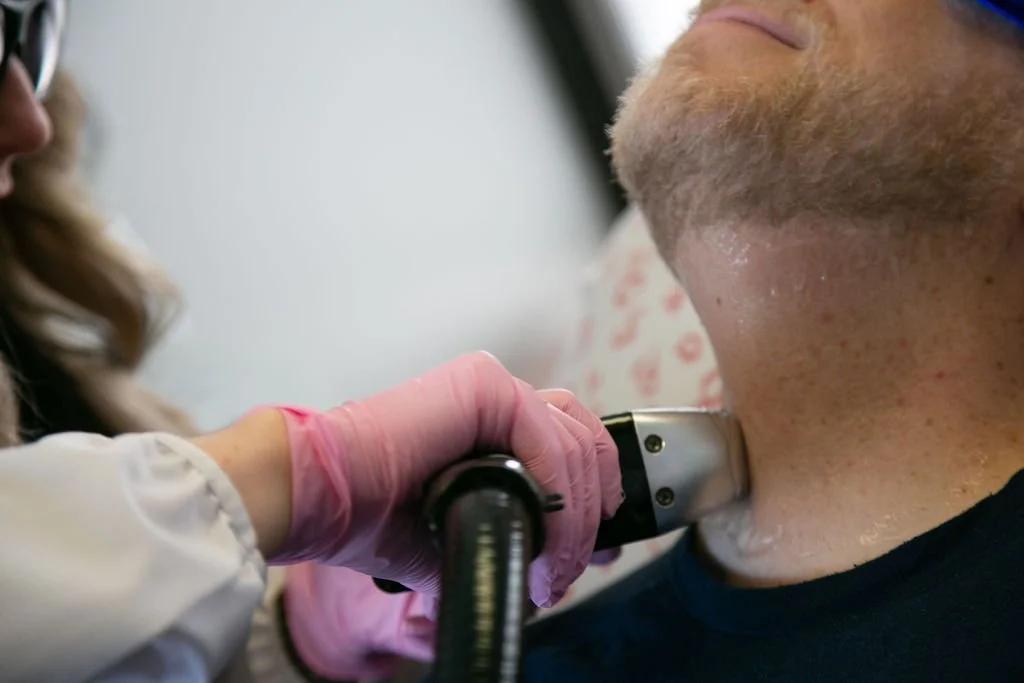 Medical professional wearing pink gloves using a ultrasound device on a patient's neck.