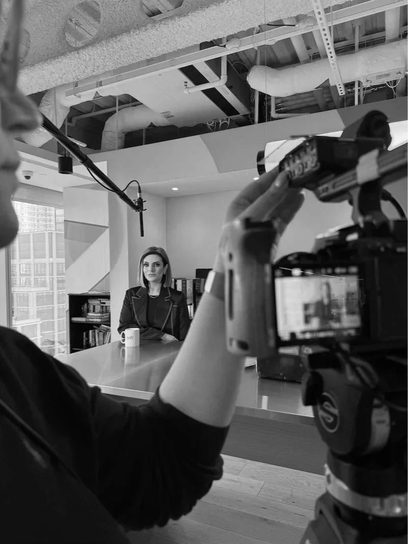 Lucy Cohen in business attire being filmed or recorded in an office setting.