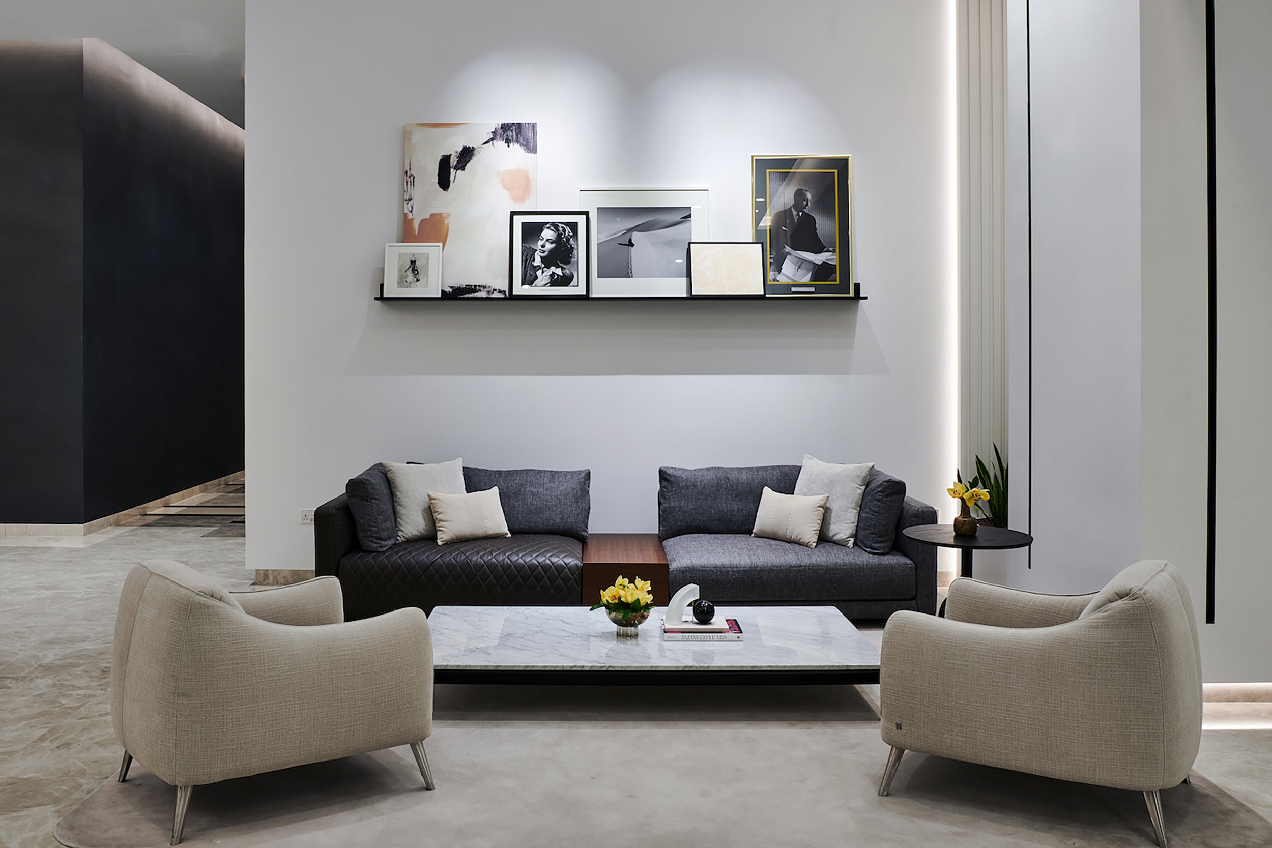 A seating area decorated with plants and books, above is a shelf containing a variety of photographs and artworks.