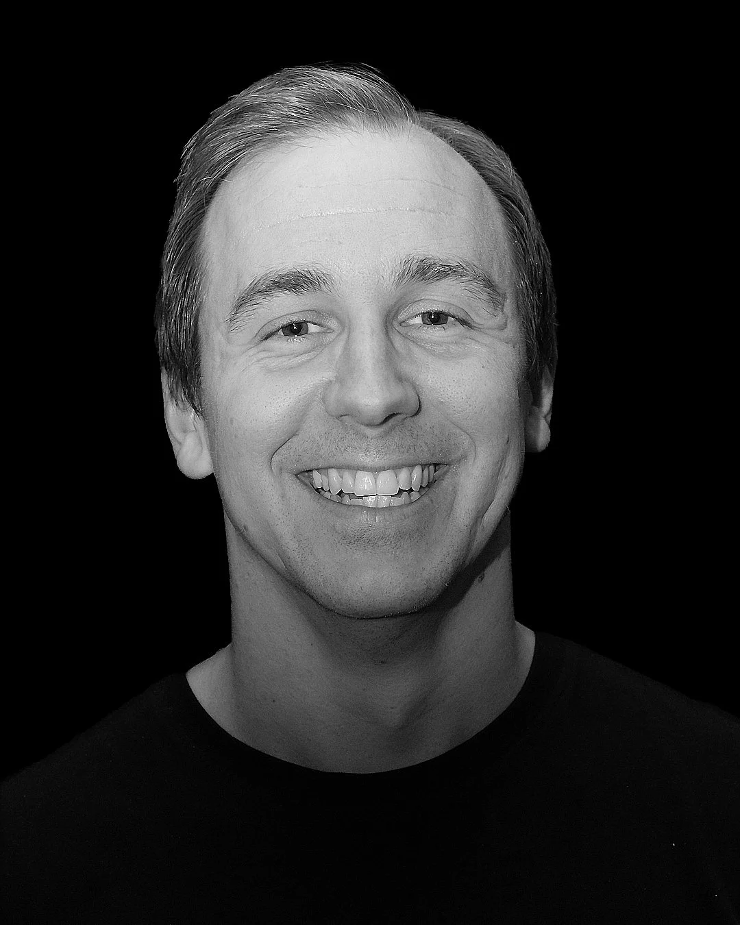 IMPROV COMEDY GBG Göteborg impro Man på scen, gestikulerar, med mikrofon framför sig, i en mörk pub eller scenmiljö med röd sammetstapet och skylt som säger 'Comedy' i bakgrunden.