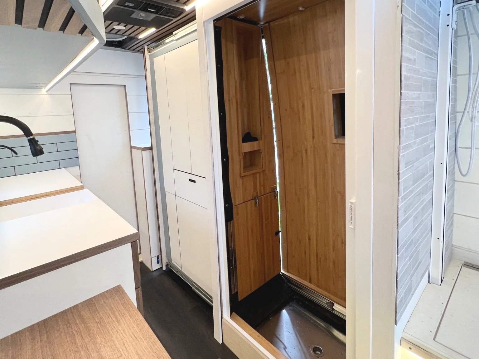 Interior of a tiny house or mobile home under construction, with an unfinished wooden floor and a closed door at the end.