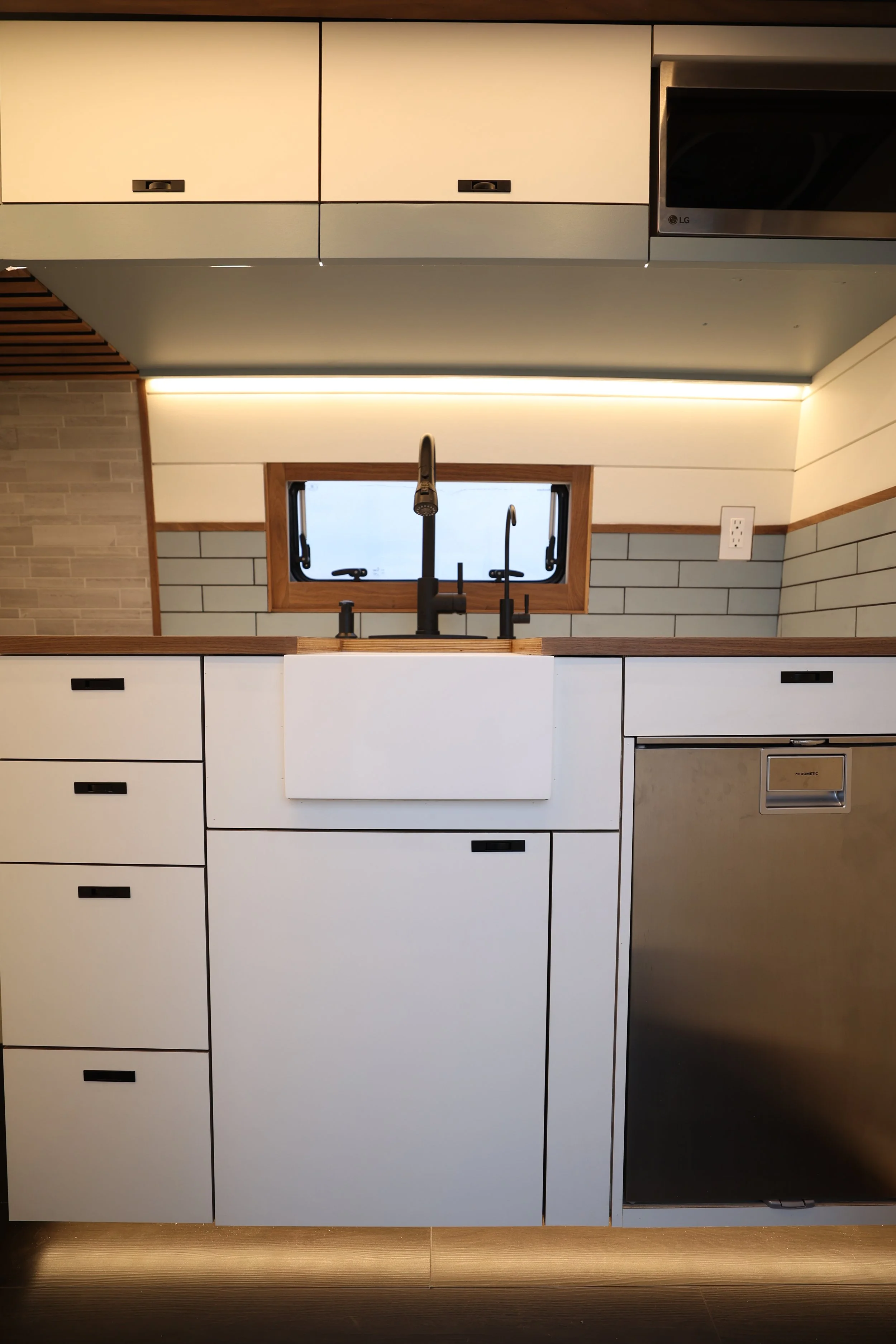 Modern kitchen with white cabinetry, a farmhouse sink, black faucet, stainless steel dishwasher, and a small window above the sink.