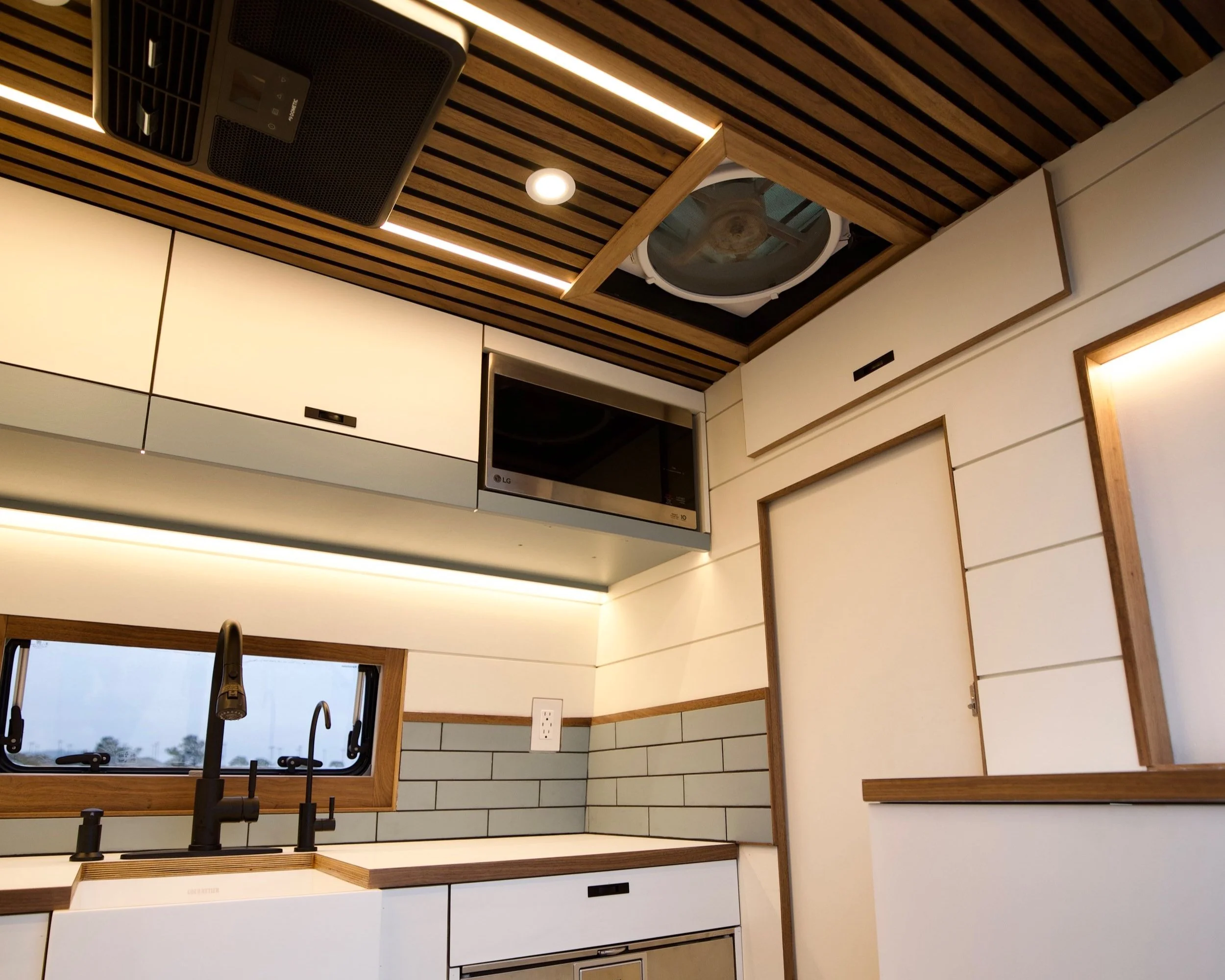 Modern kitchen with white cabinets, black faucet, gray tiled backsplash, wooden trim, and ceiling with wooden slats and built-in lighting.
