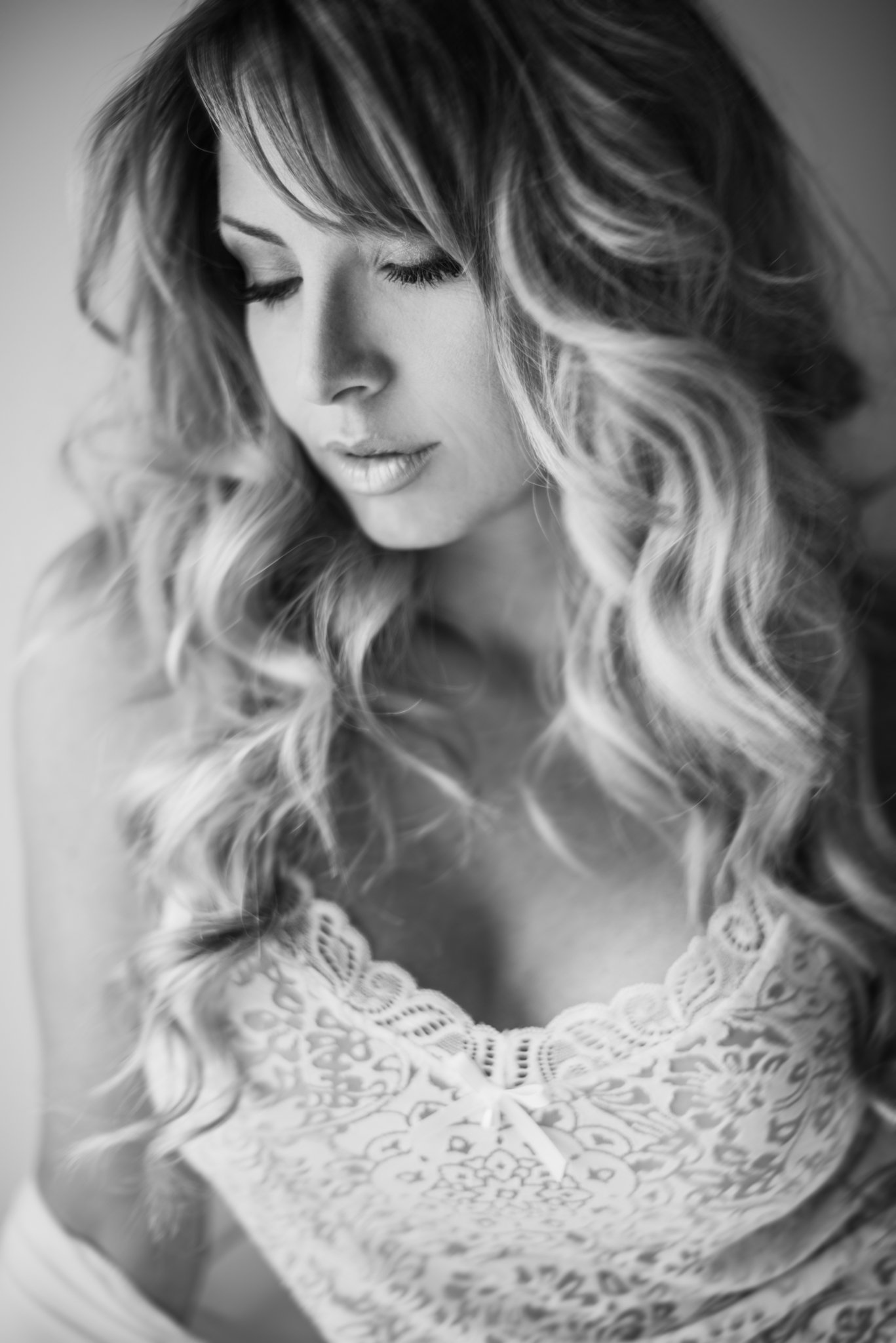 Black and white close-up of a woman with light, wavy hair, eyes closed, wearing a lacy top.