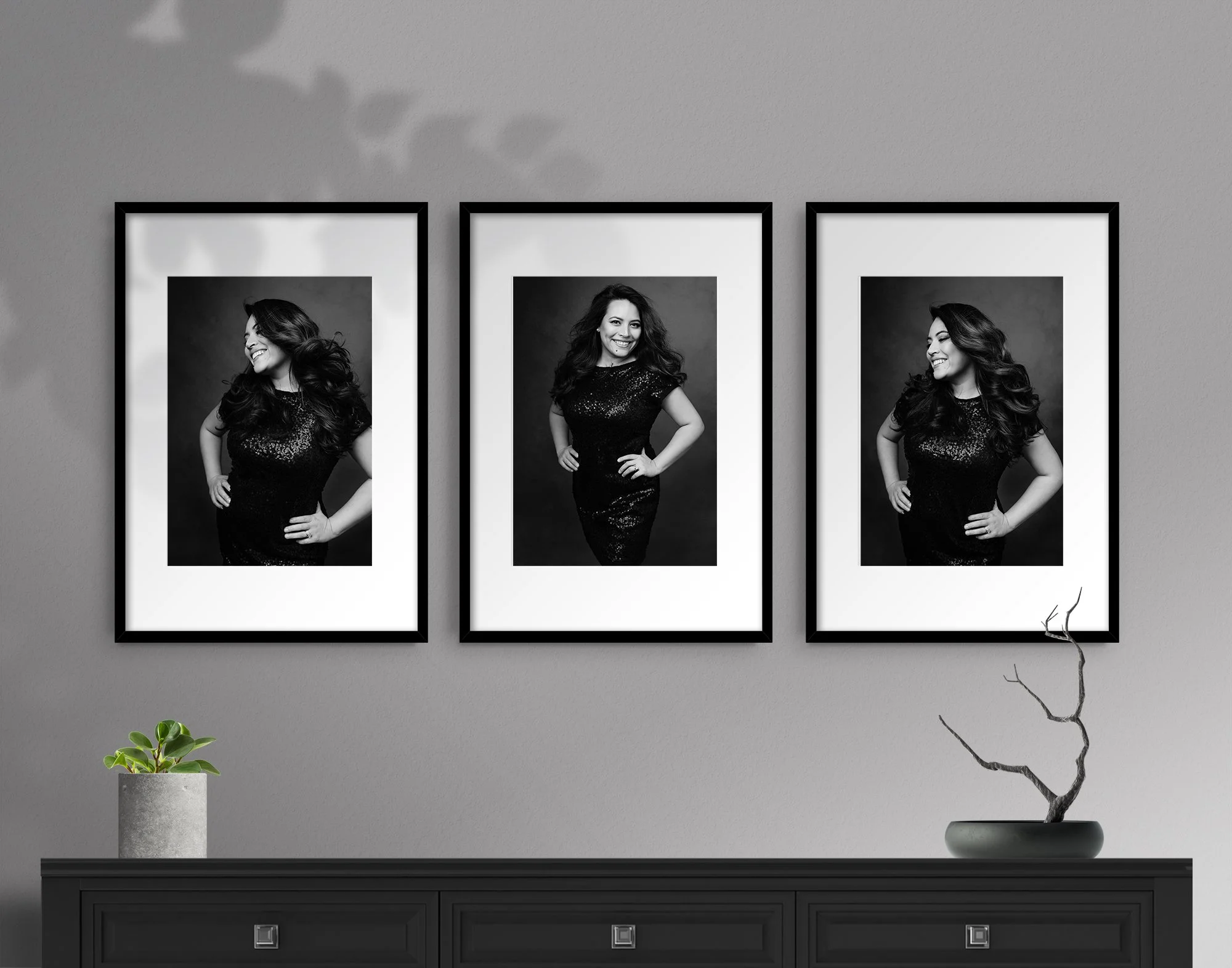 Three black and white portraits of a woman in a sequin dress, smiling and posing with her hands on her hips, hung on a gray wall above a black cabinet with a small potted plant and a decorative branch.