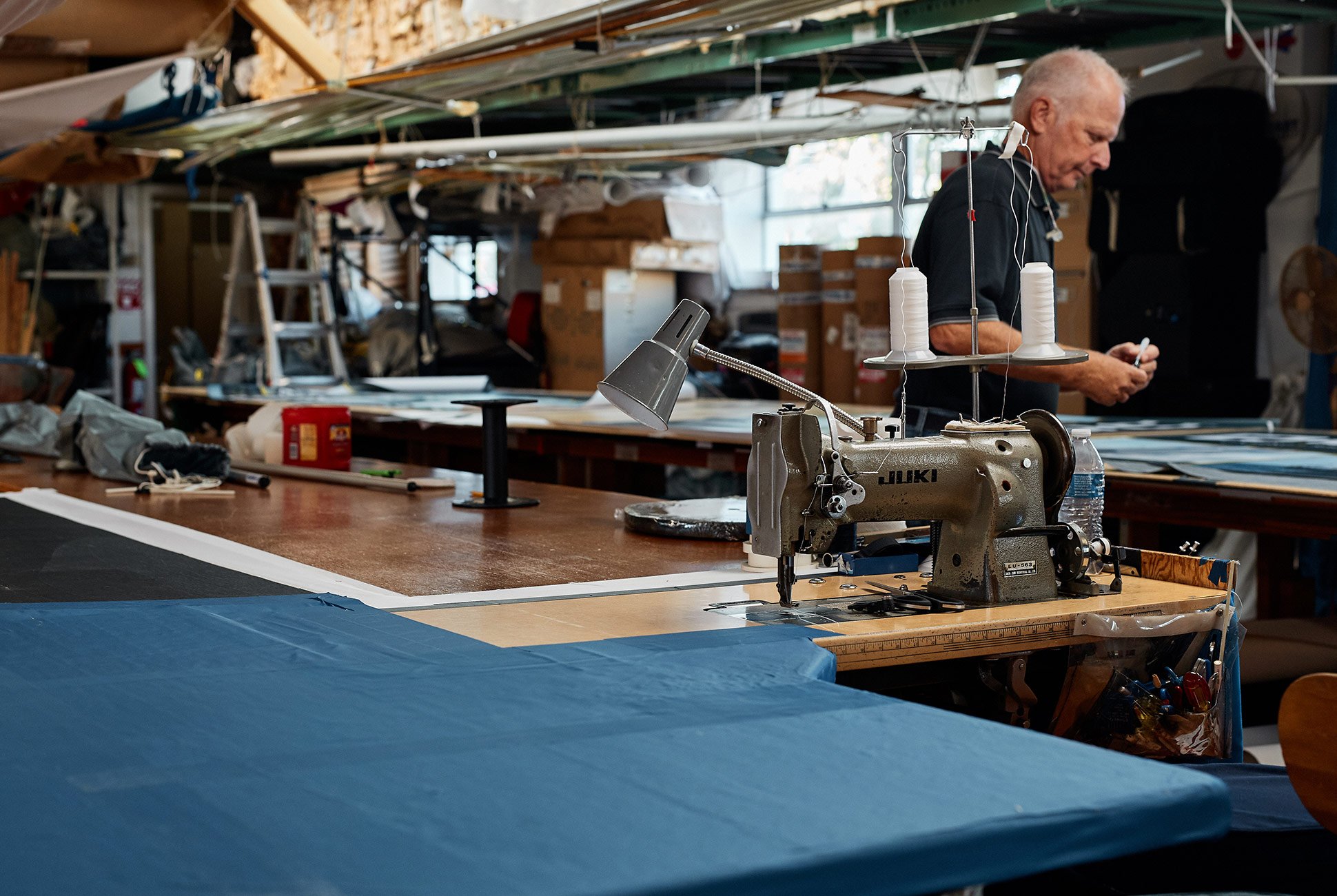 a factory with a few people working and a sewing machine set up near blue fabric
