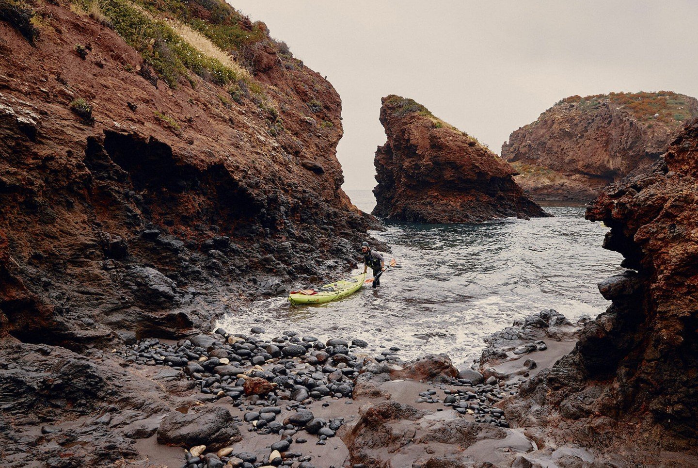 man bringing a kayak into a small lagoon by the cliffs
