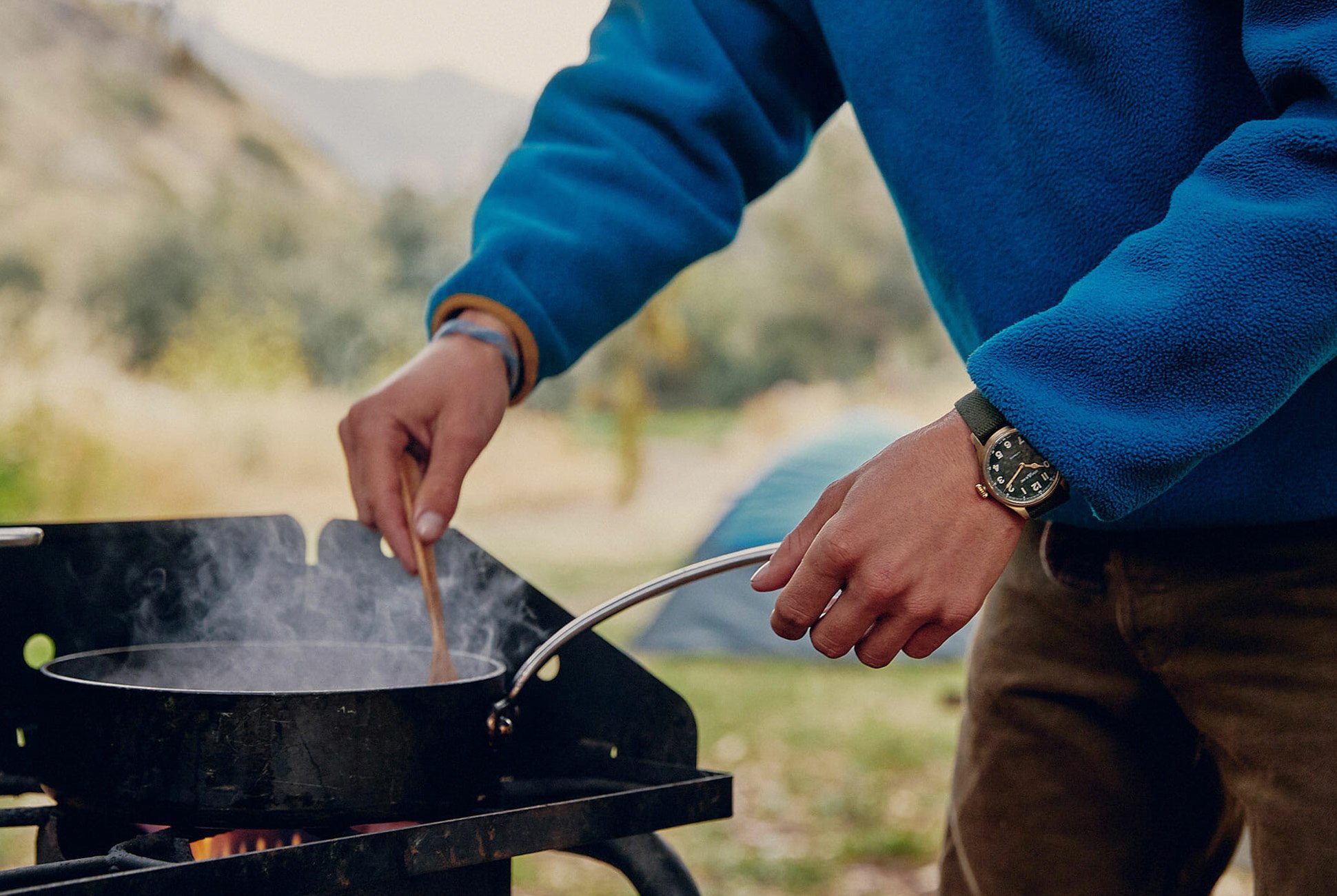 man leaning over a small pan, stirring its ingredients