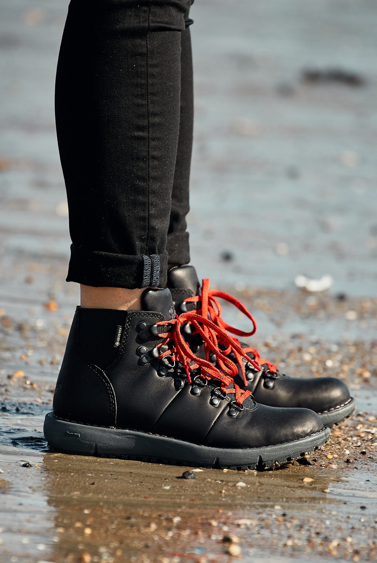 person wearing black danner boots standing on sand