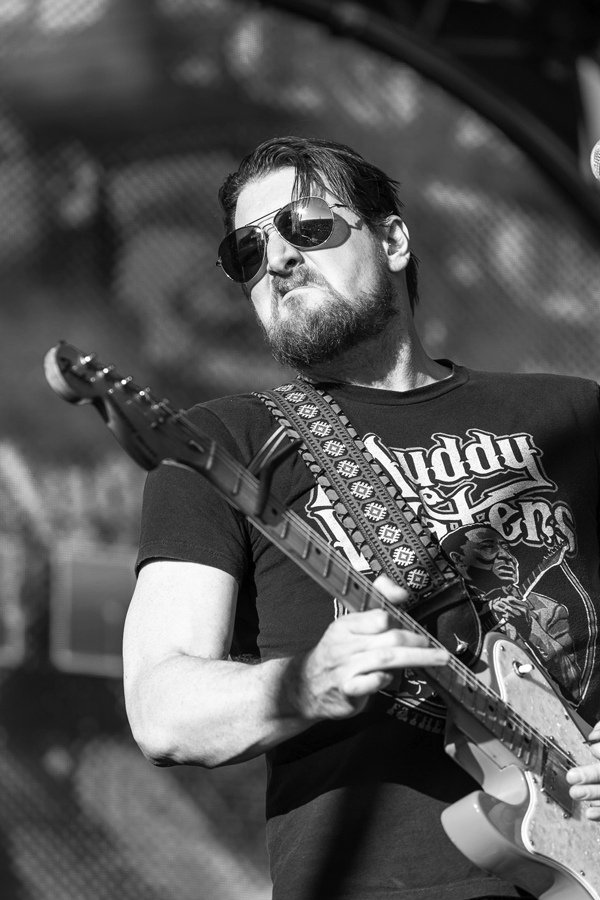 Brett Wood — Australian musician with dark hair and beard wearing sunglasses playing electric guitar outdoors