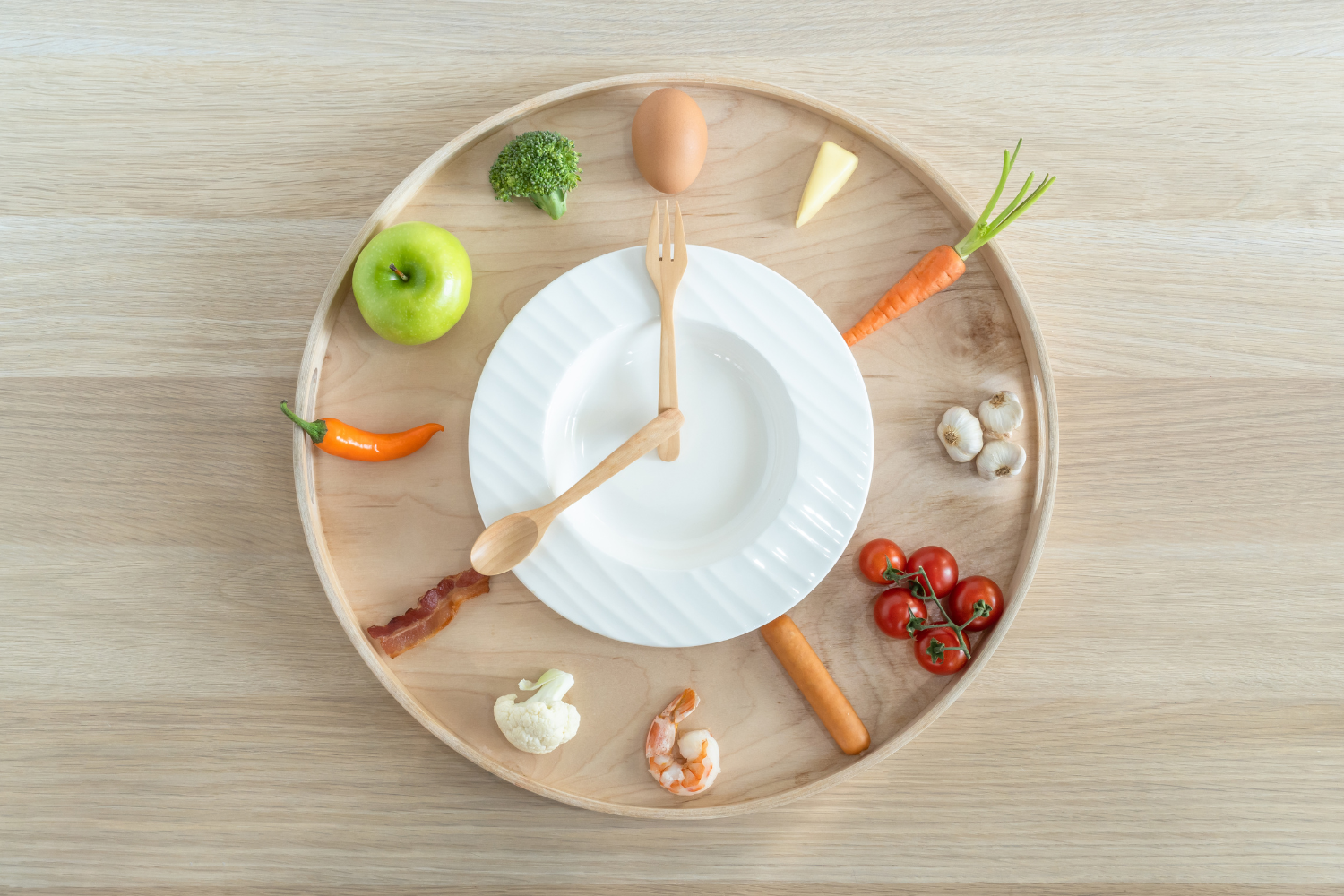 A wooden tray with a white plate and a fork and spoon in the center, surrounded by various vegetables and an egg, arranged to resemble a clock.