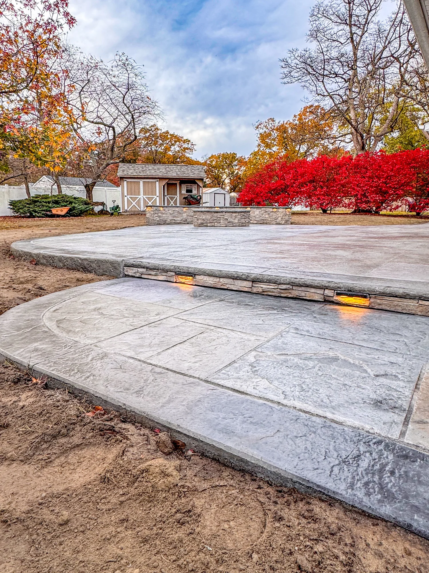 Stamped concrete outdoor living patio with gas fire pit, stone veneer seating walls, and LED landscape lighting in Cherry Hill NJ by Patrick Breen Masonry