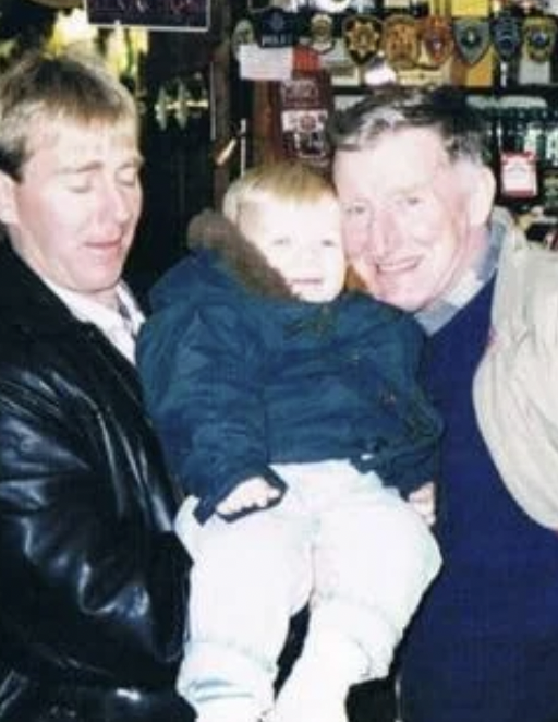 Three people, two men and a young child, are smiling and posing together inside a store with various patches and badges displayed on the wall behind them.