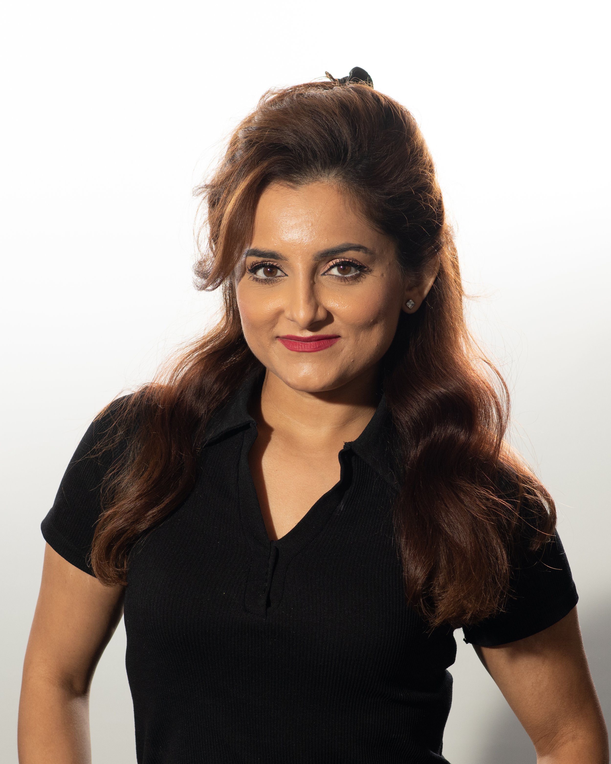 A woman with long brown hair, wearing a black collared shirt, smiling at the camera against a plain white background.