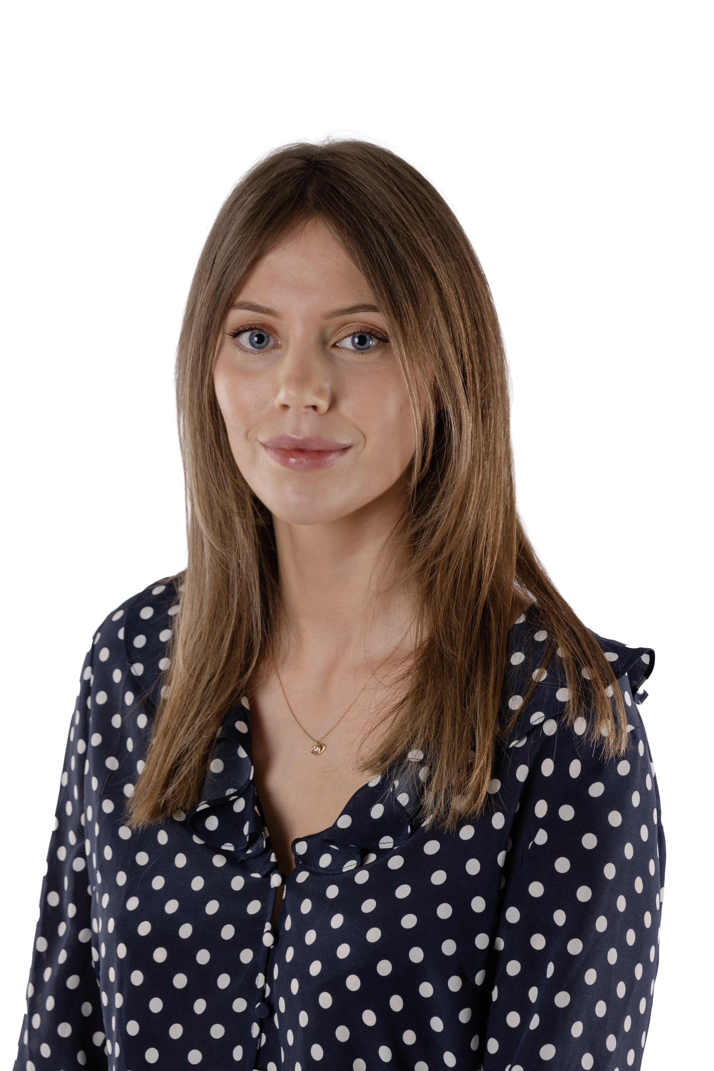 A woman with straight, shoulder-length brown hair and blue eyes, wearing a navy blue polka dot blouse and a delicate gold necklace, posing against a white background.