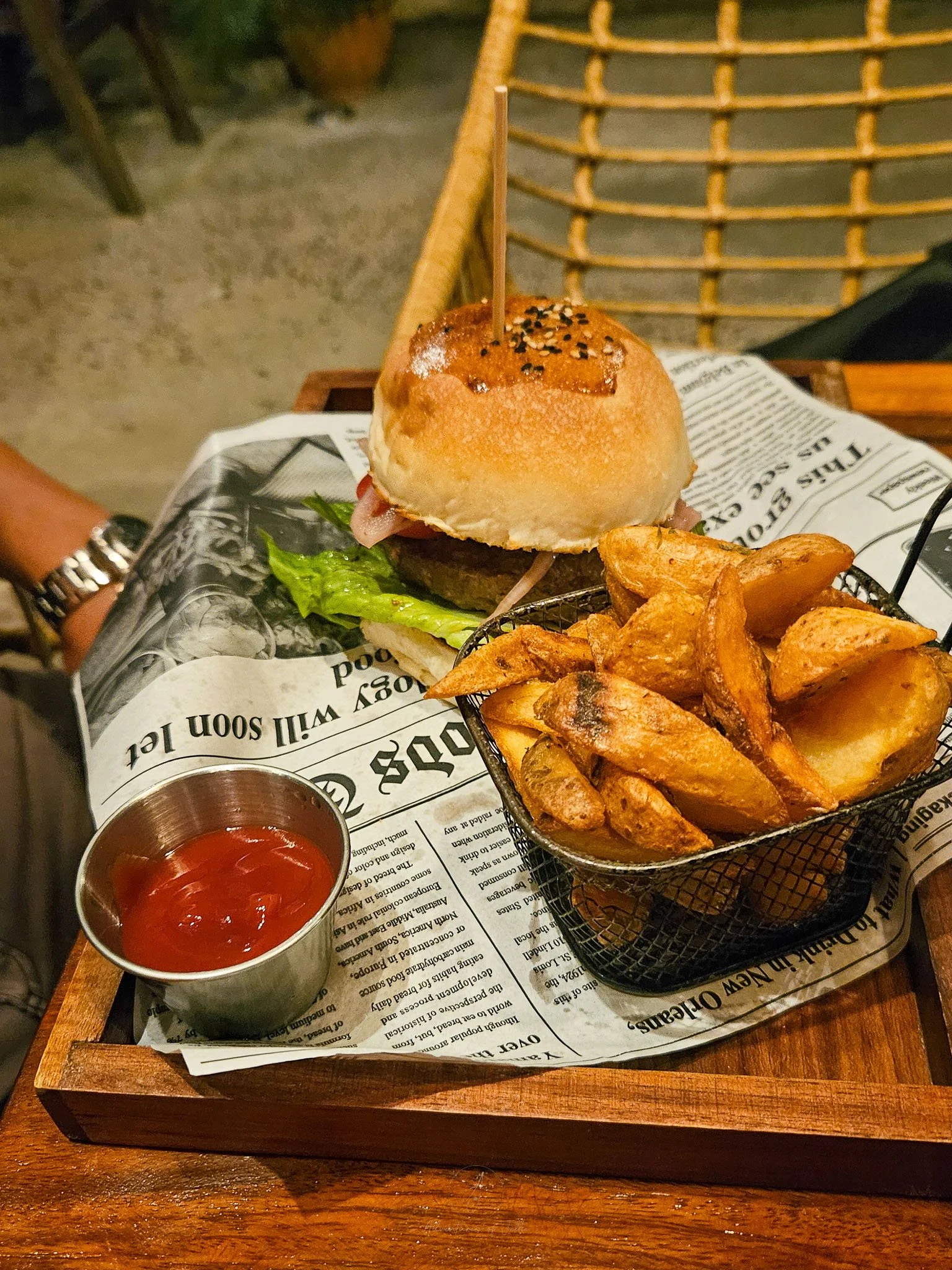 Sitting on a wooden tray covered in newspaper sits a beef burger, a basket of potato fries and a ramekin of tomato ketchup at the Mythai Burger restaurant in Koh Phangan.