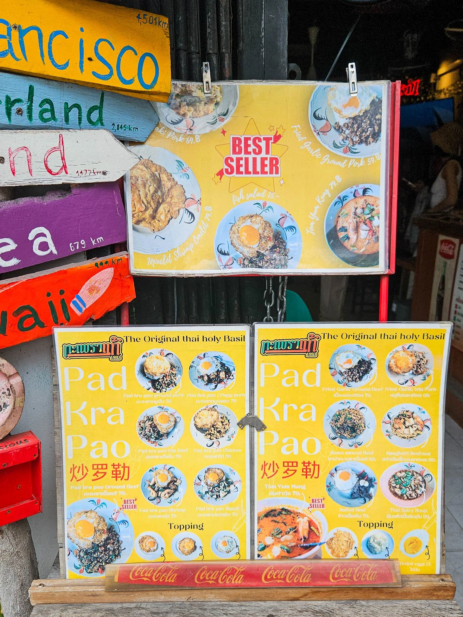 A laminated yellow menu is displayed showing the different pad kra pao options available at Bangkok's Original Pad Kra Pao restaurant.