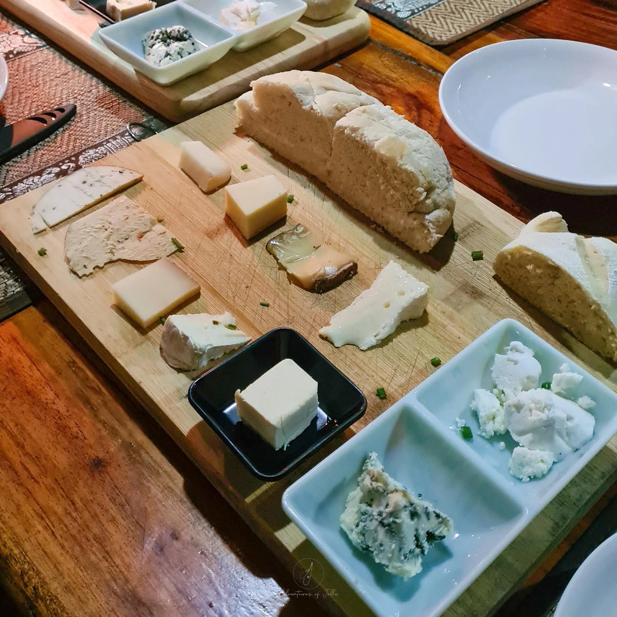 A wooden cheese board is filled with slices of cheese (both hard and soft cheeses) and a slice of baguette at the Pizza Pasta Restaurant in Nong Khiaw.
