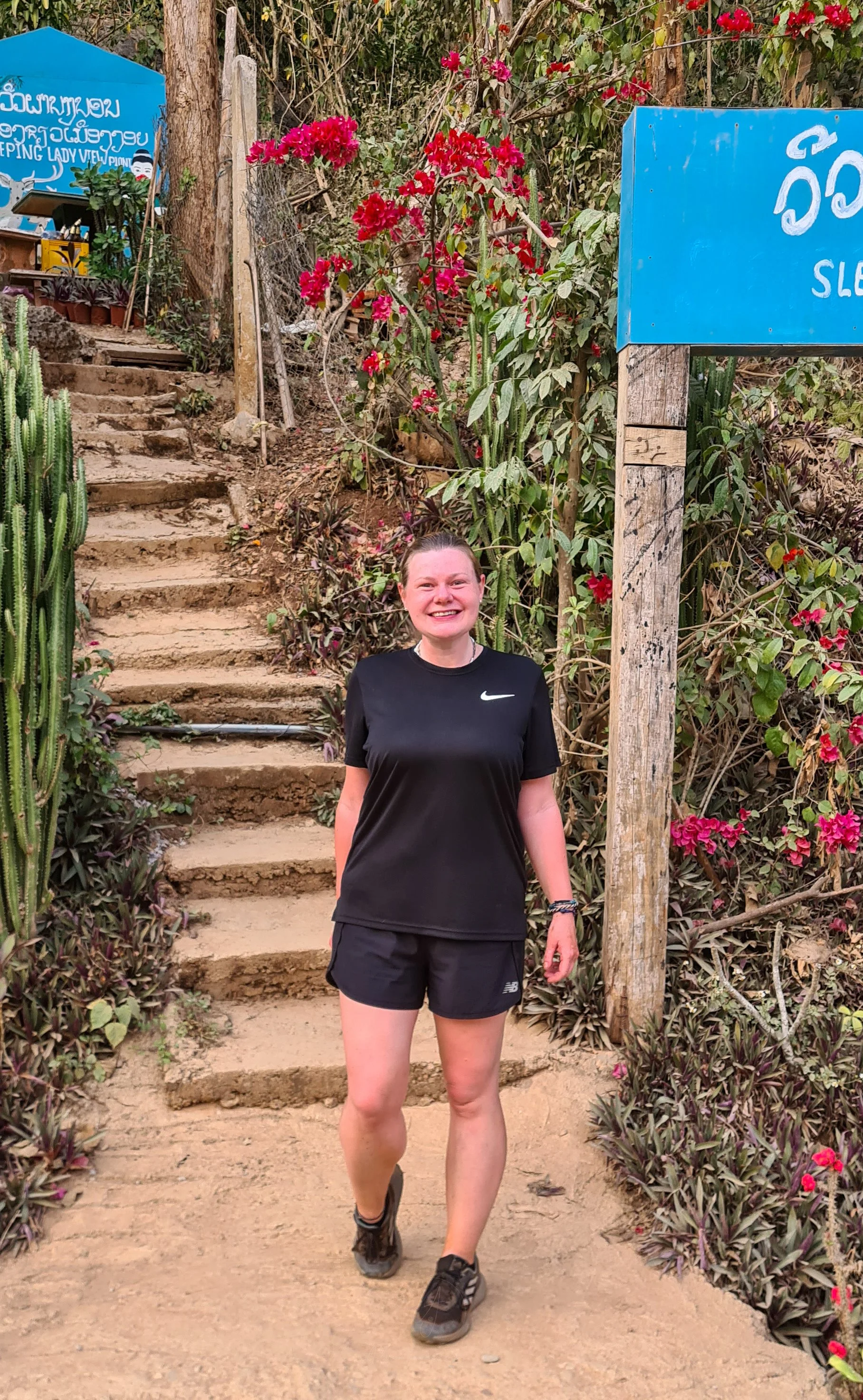 Ellie poses at the entrance to the Sleeping Lady Viewpoint in Nong Khiaw. She is wearing black shorts, a black t-shirt and trainers.