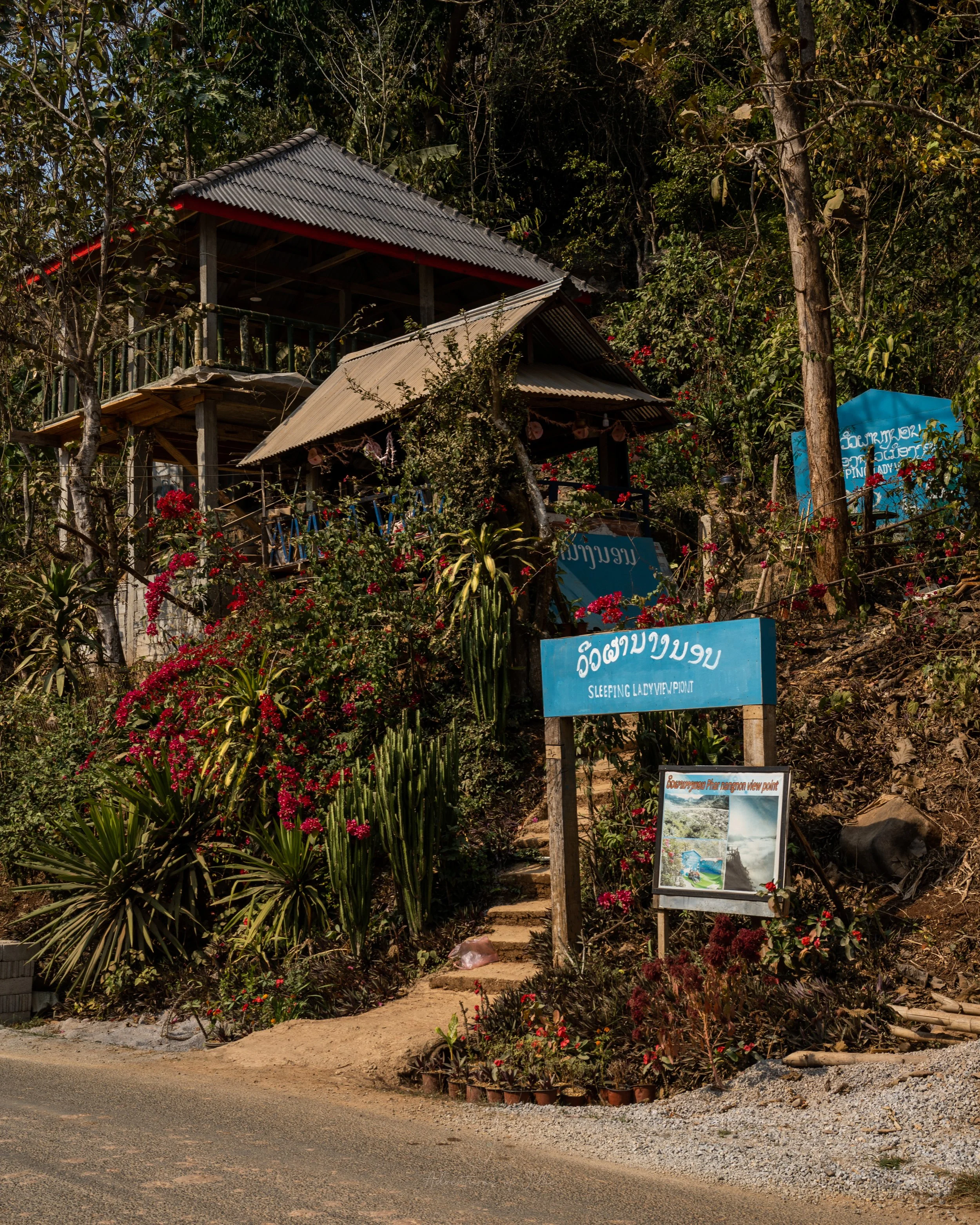 A blue sign and steps leading up marks the entrance for the ticket booth to the Sleeping Lady hike in Nong Khiaw, Laos.