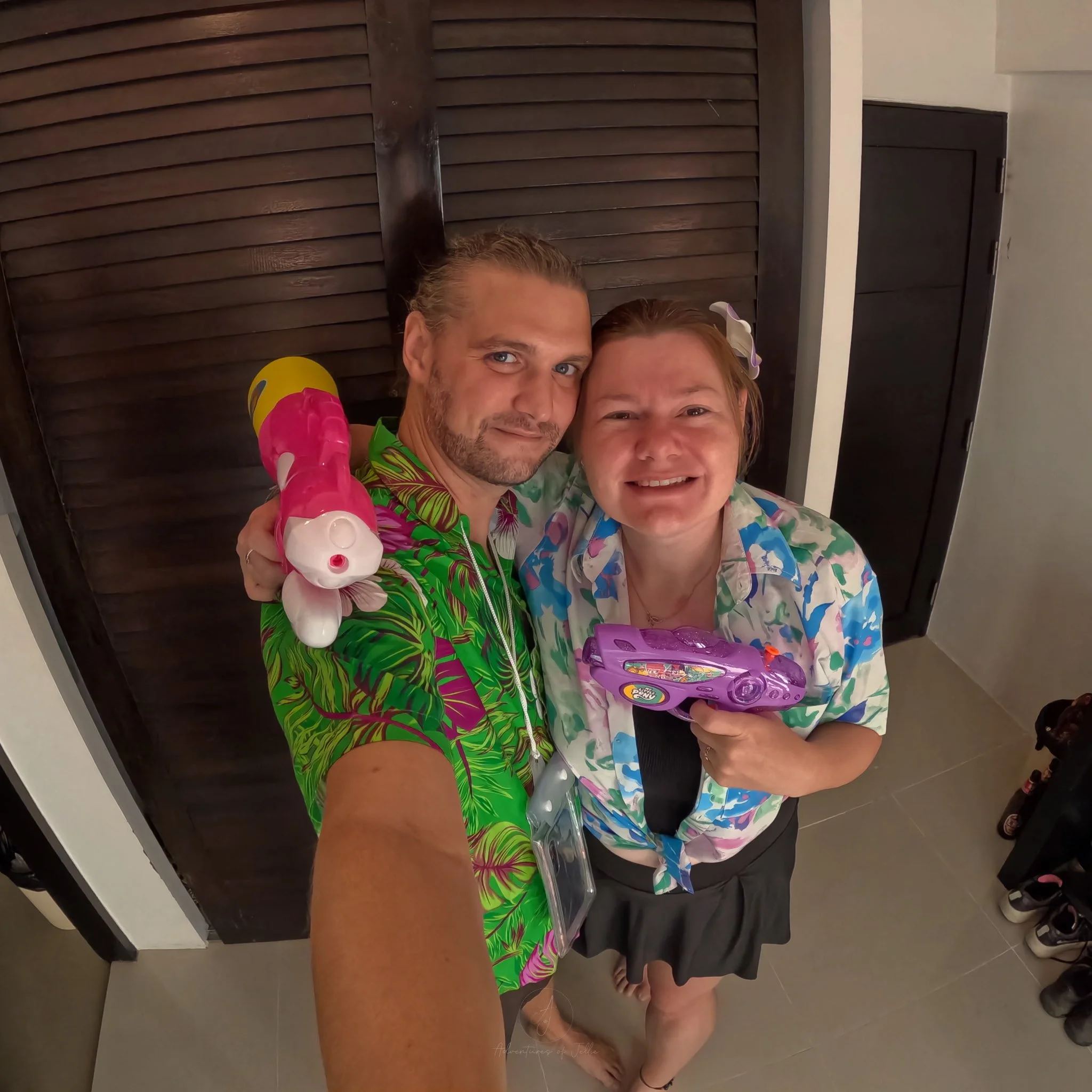 John and Ellie pose in vibrant shirts. John is in a neon green and purple leaf print, Ellie is in pink blue and green petals.